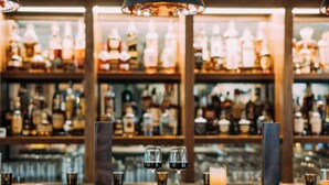 Un espace bar avec un plafond en bois, des tabourets de bar et une variété de bouteilles et de verres exposés sur des étagères.