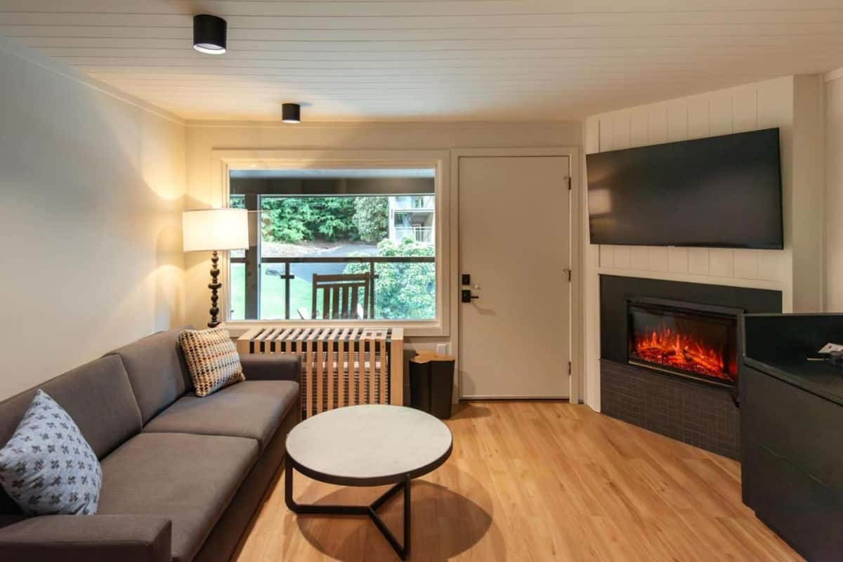 A cozy living room with a sofa, a round table, a fireplace, and a TV mounted on the wall.