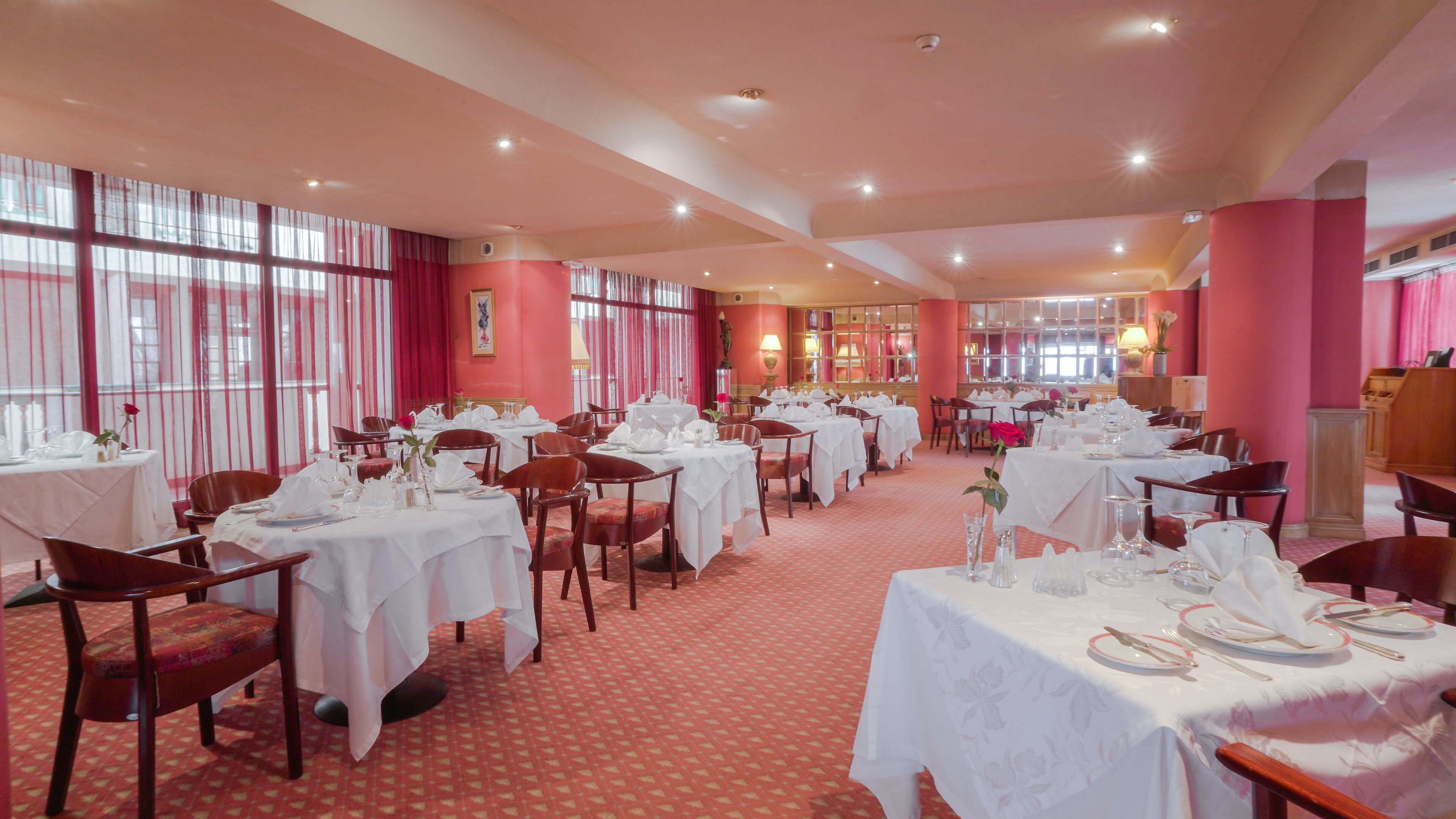 A restaurant with multiple tables set for dining, featuring a red carpet and white tablecloths.