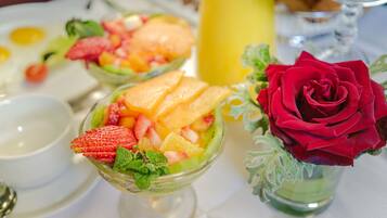 Una mesa puesta con una ensalada de frutas, una rosa y un vaso de jugo.
