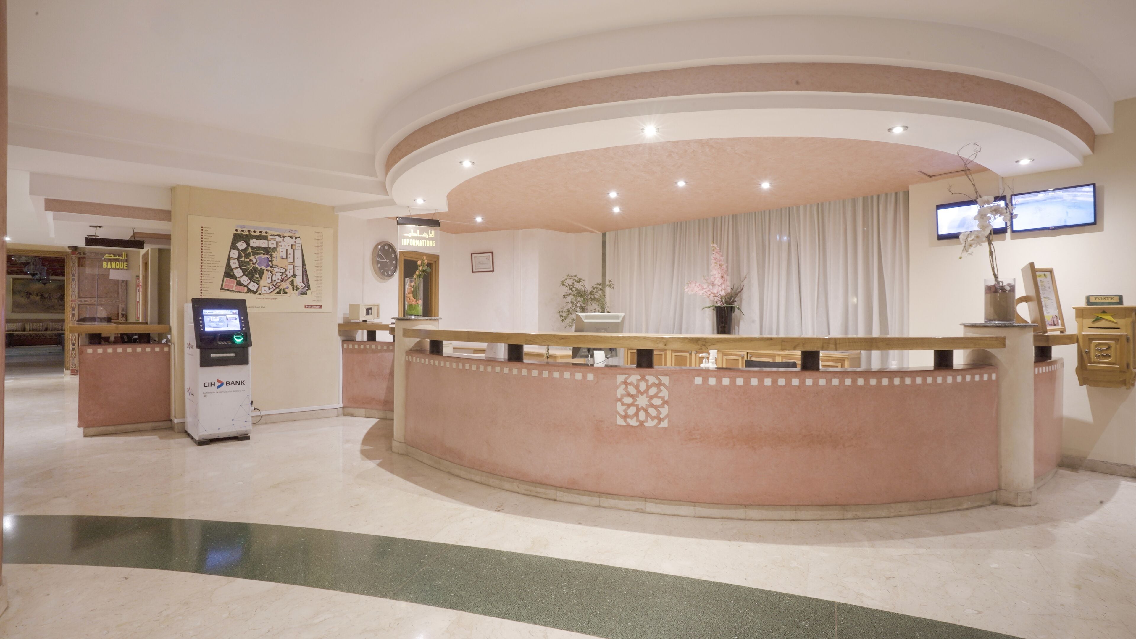 A hotel reception area with a curved reception desk, a digital kiosk, a clock, and a map on the wall.