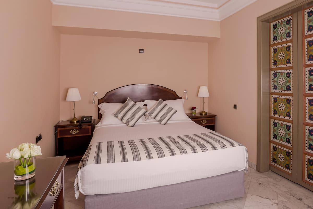 A neatly made bed with striped bedding, two bedside lamps, a nightstand with a phone, and a vase with flowers.