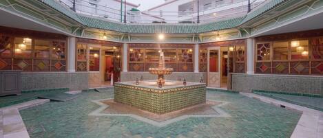 Een ruime atrium met een fontein in het midden, versierde betegelde vloeren en een hoog plafond met dakramen.