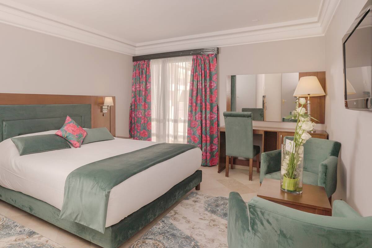 A hotel room with a bed, a desk, a chair, a mirror, and a lamp.