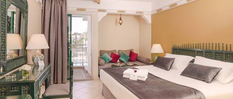 A hotel room with a bed, a sitting area with a sofa, a table with a lamp, and a decorative mirror.