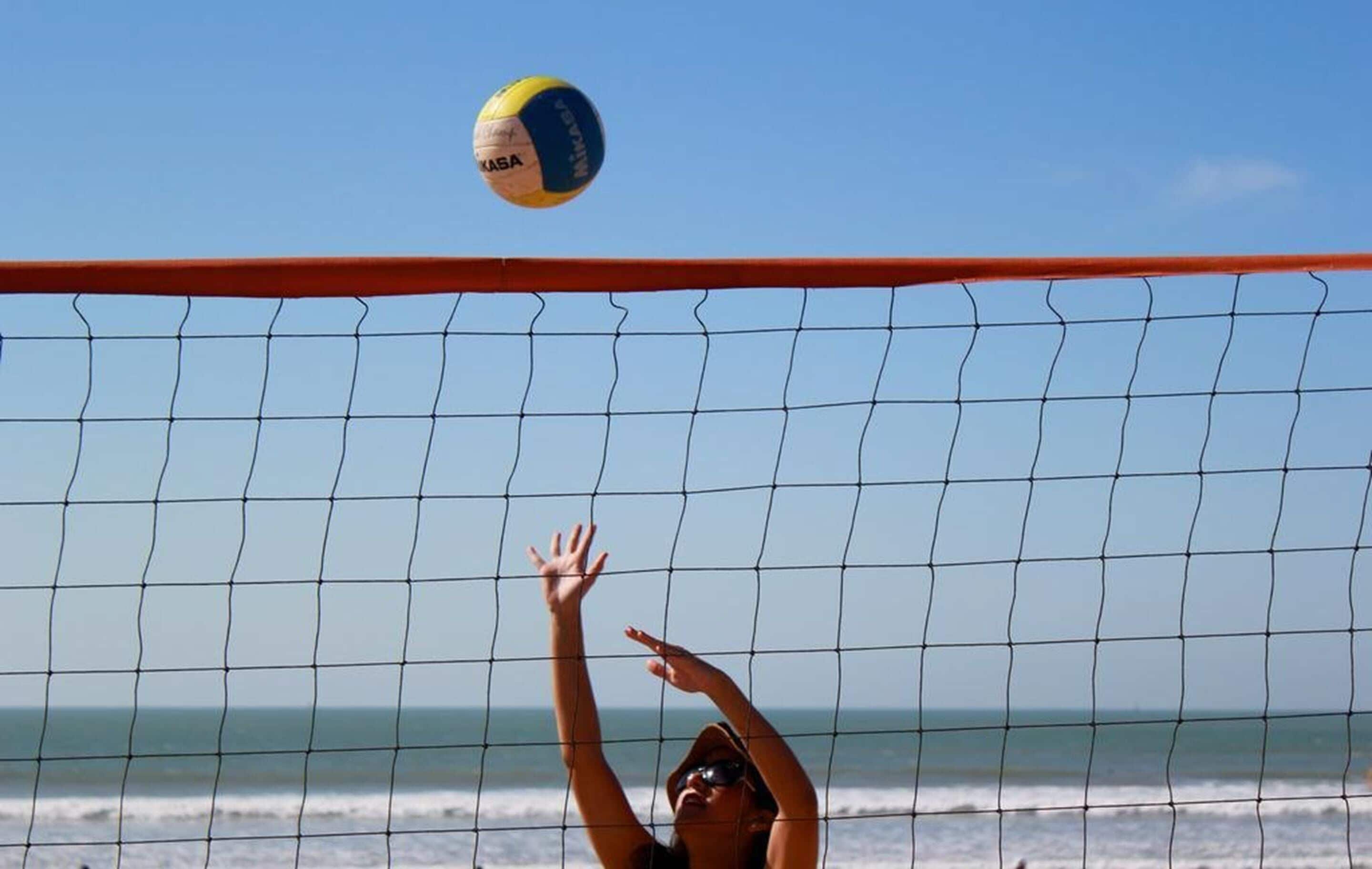 A beach volleyball game with a net and a player reaching for the ball.