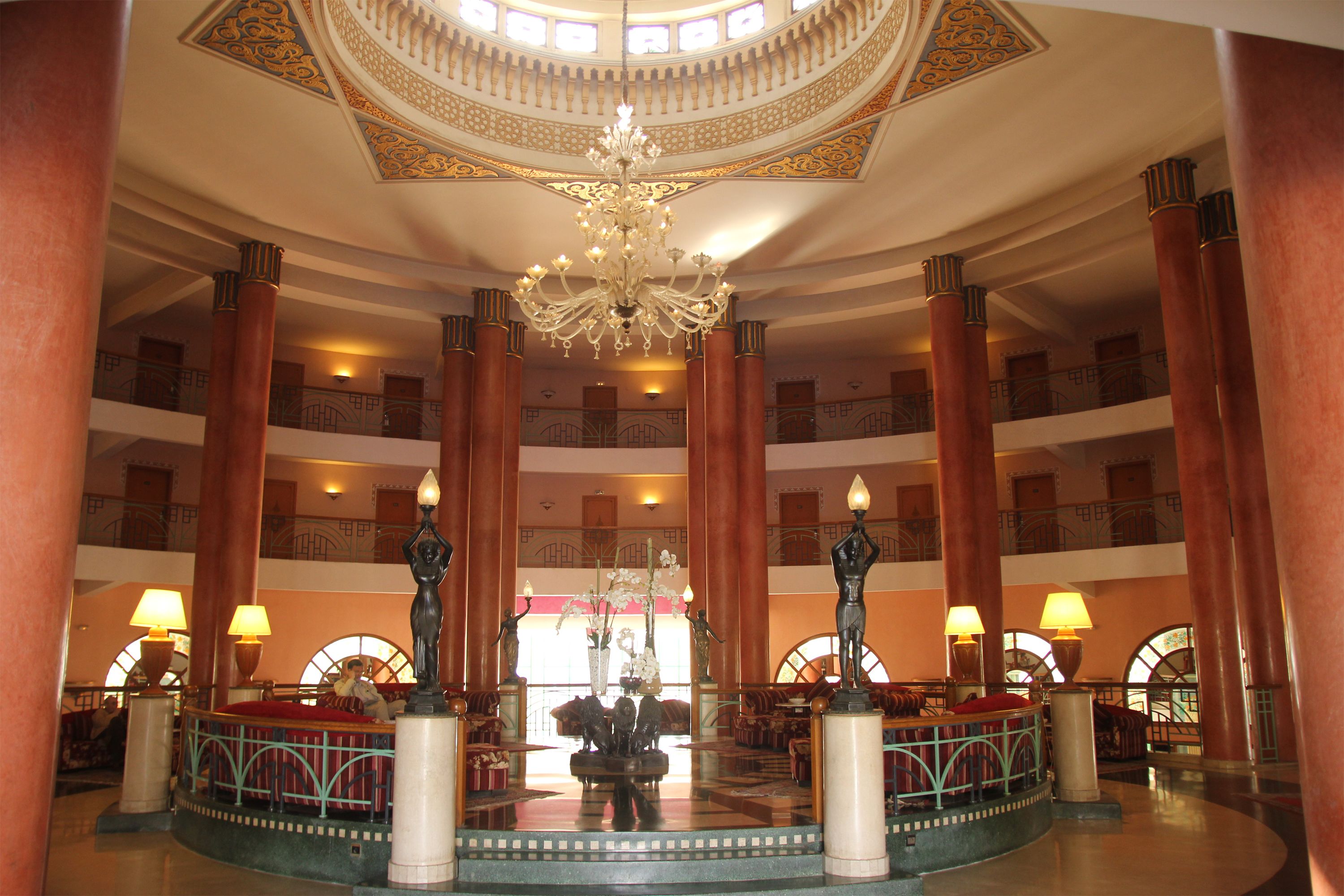 A grand lobby with a central fountain, ornate columns, and a chandelier.