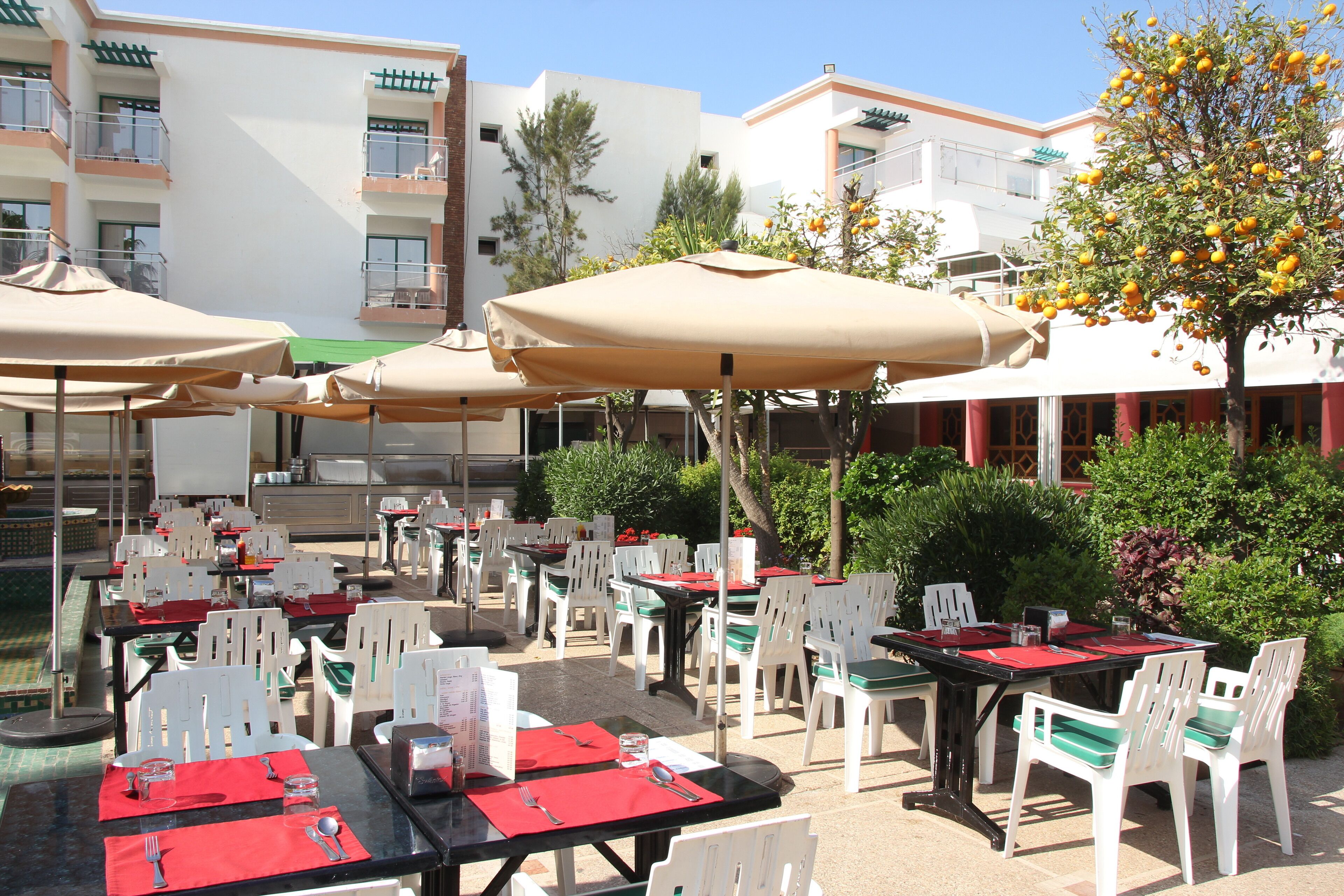 An outdoor dining area with tables and chairs, umbrellas, and a building in the background.