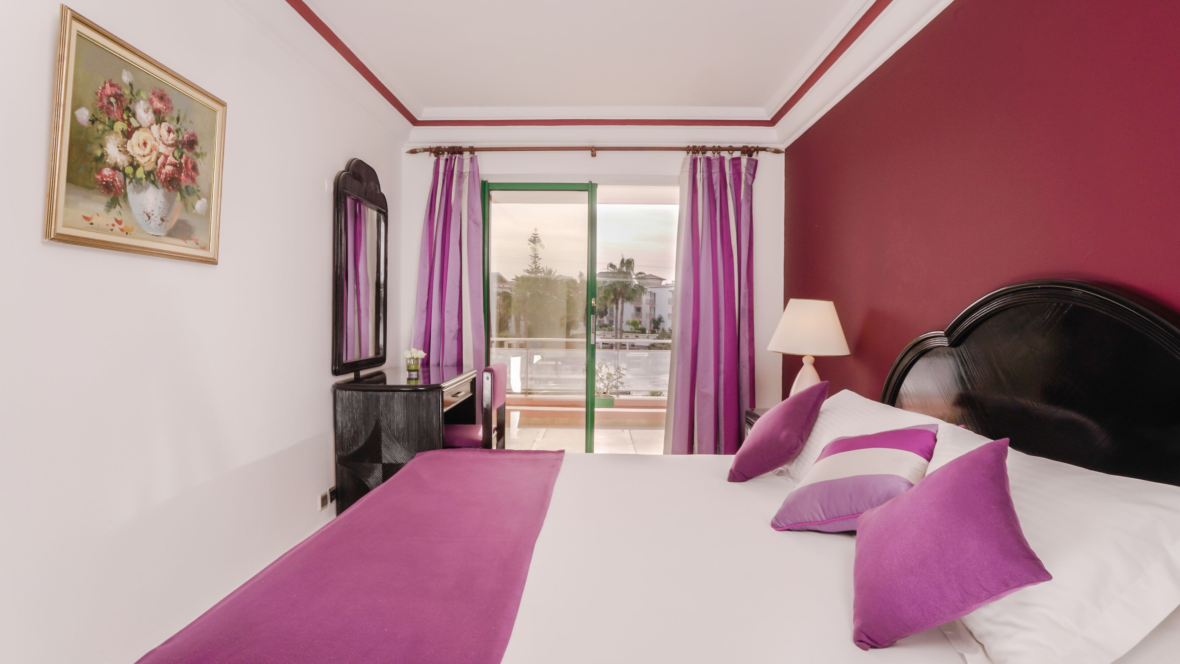 A bedroom with a bed, a desk, a chair, a mirror, and a window with curtains.