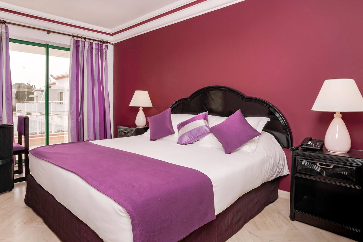 A hotel room with a bed, two bedside tables, a chair, and a view of the outside.