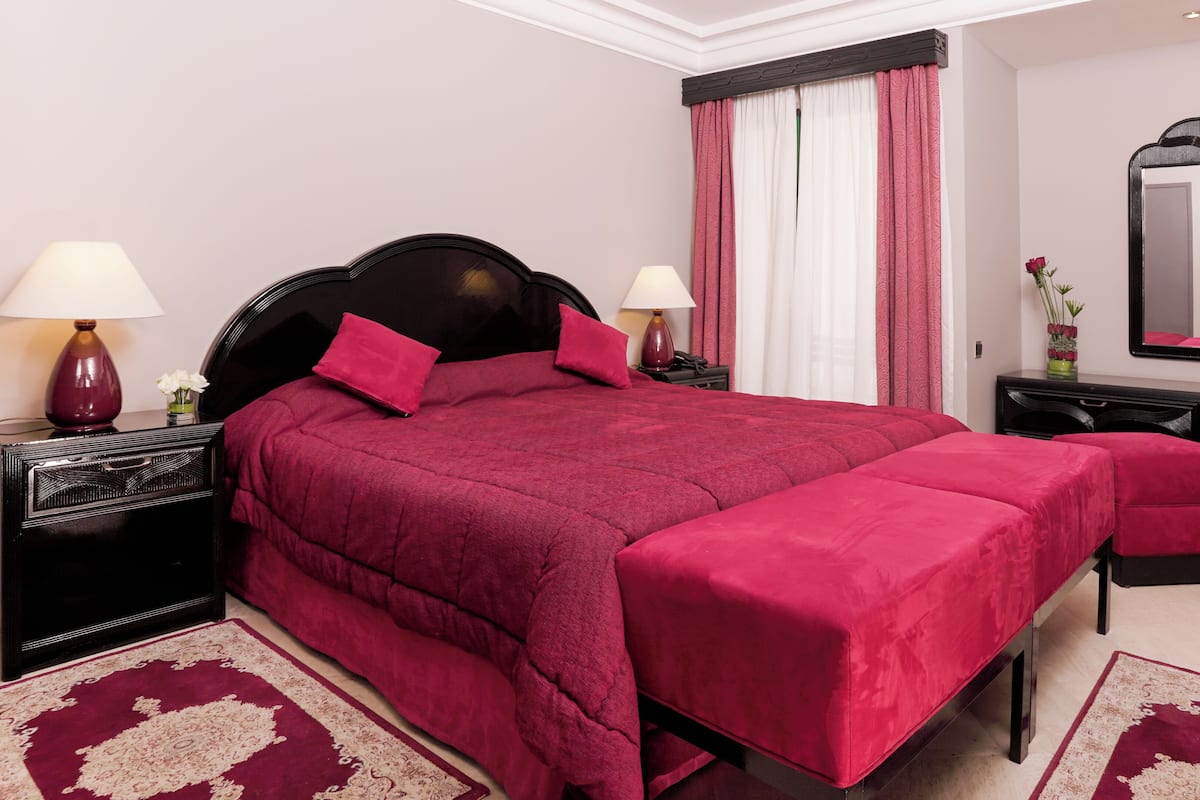 A bedroom with a large bed, two bedside tables, a dresser, a mirror, and a window with curtains.