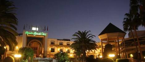 A hotel entrance with a sign reading "Grand Oasis Club," a fountain, palm trees, and a gazebo.