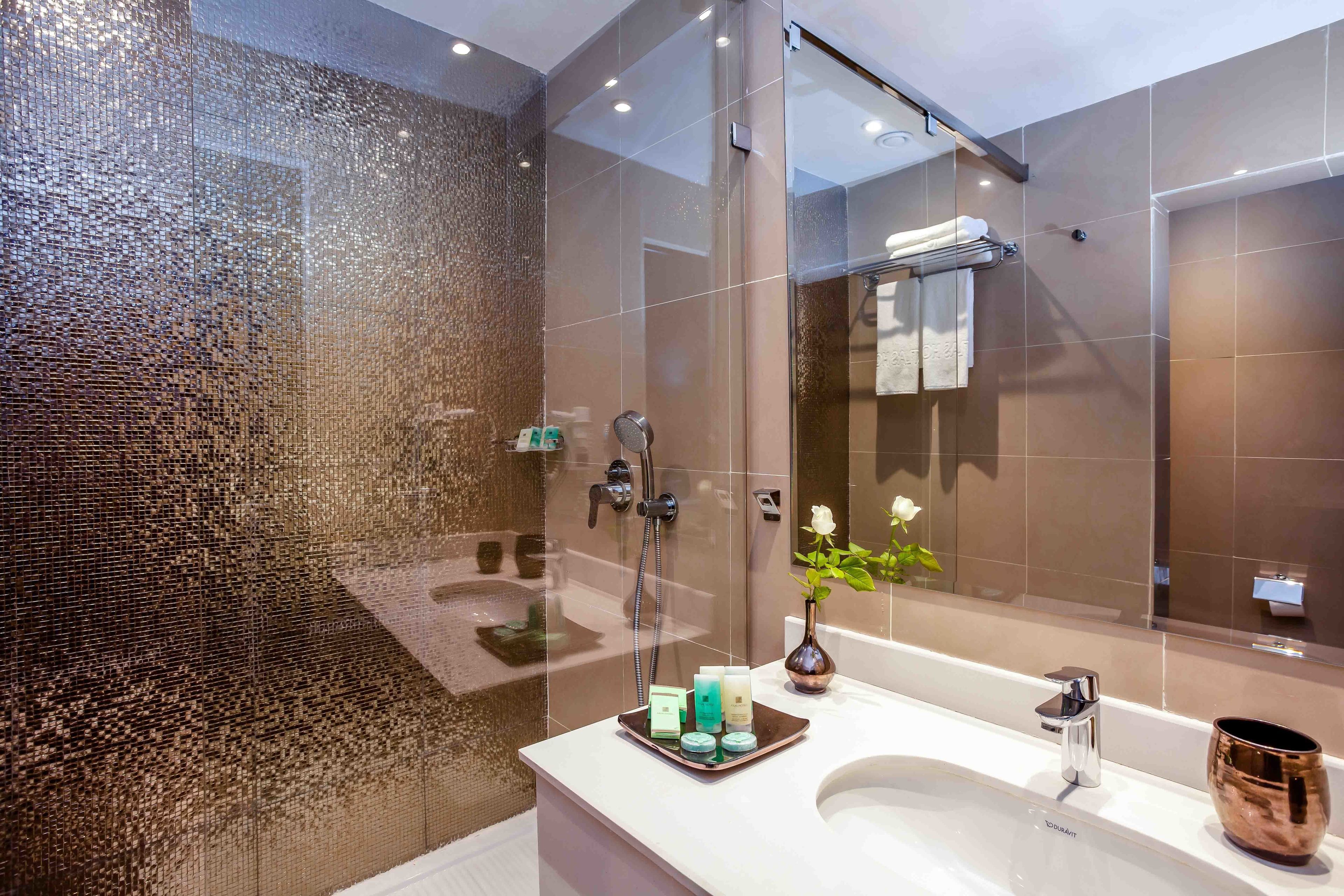 Un baño moderno con cabina de ducha de vidrio, lavamanos blanco y un espejo grande.