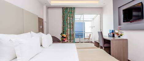 Una habitación de hotel con una cama grande, un escritorio con una silla, un televisor montado en la pared y un balcón con vistas al mar.