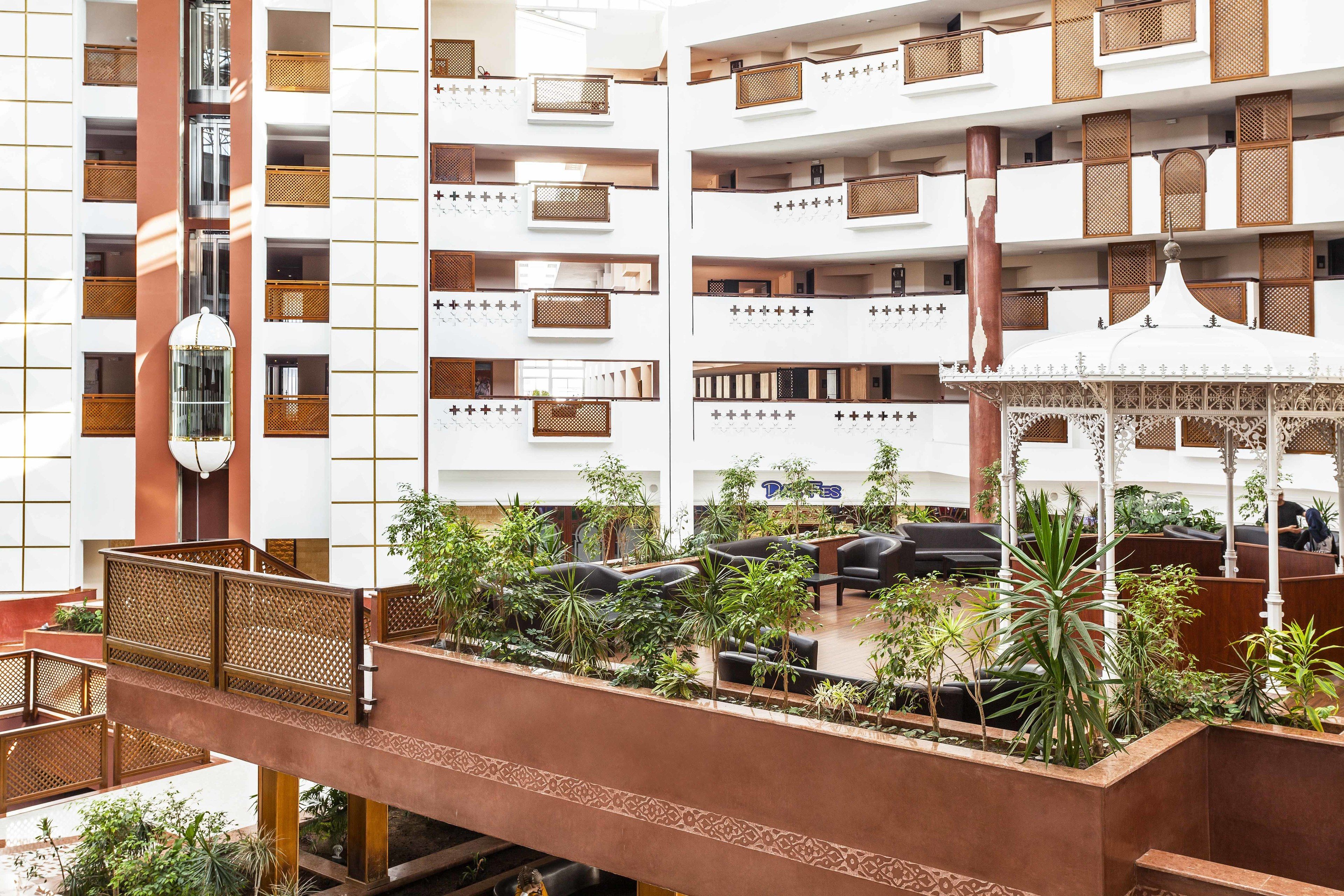 Un hall d’hôtel à plusieurs niveaux, doté d’un atrium central, de balcons et d’un espace détente agrémenté de plantes.