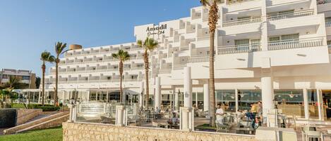 Un hotel moderno con varios balcones, zonas de estar al aire libre y palmeras.