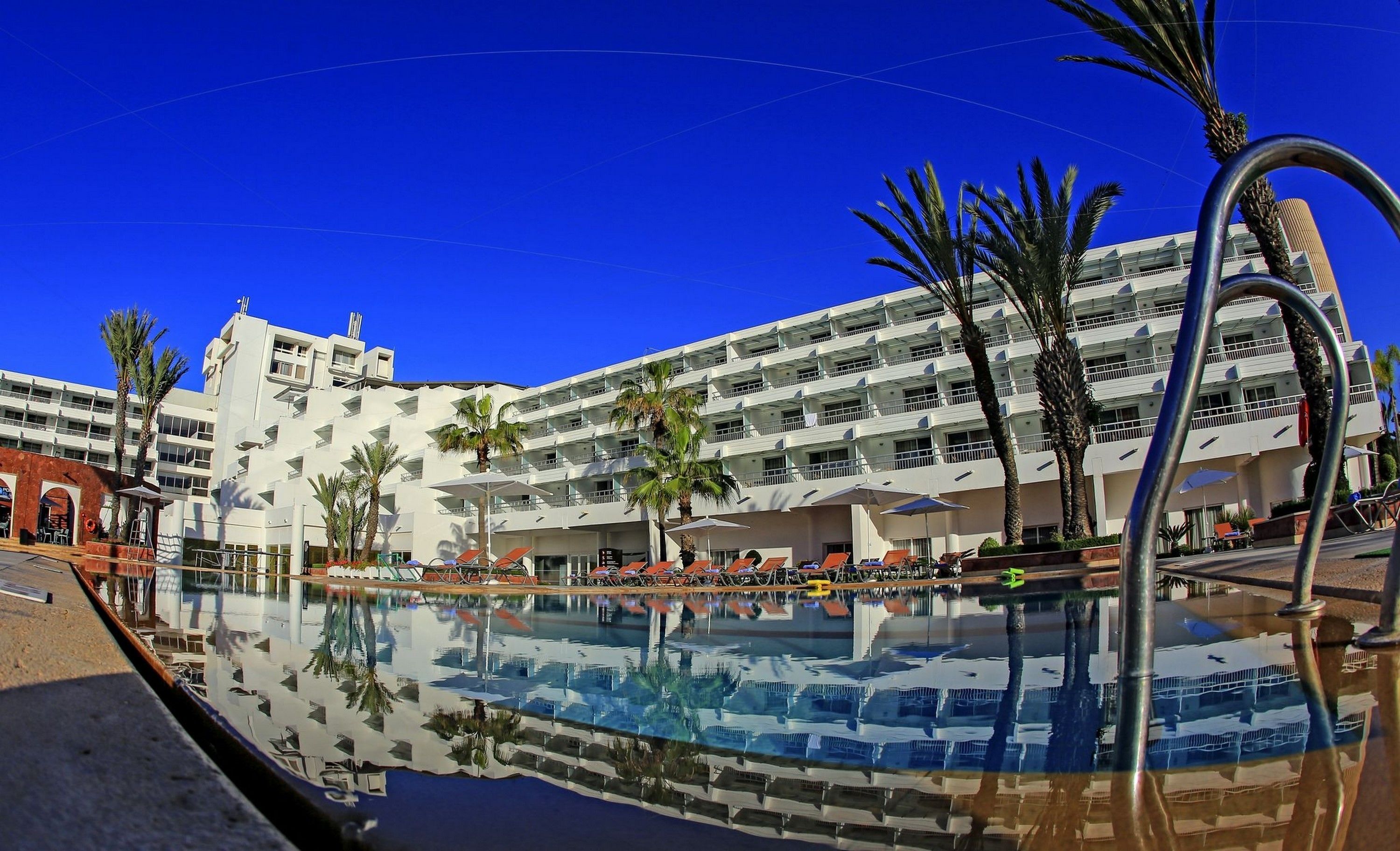 Un hotel con una piscina grande, varios balcones y palmeras.