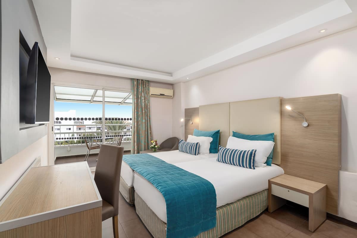 A modern hotel room with a large bed, a desk, and a balcony with a view.