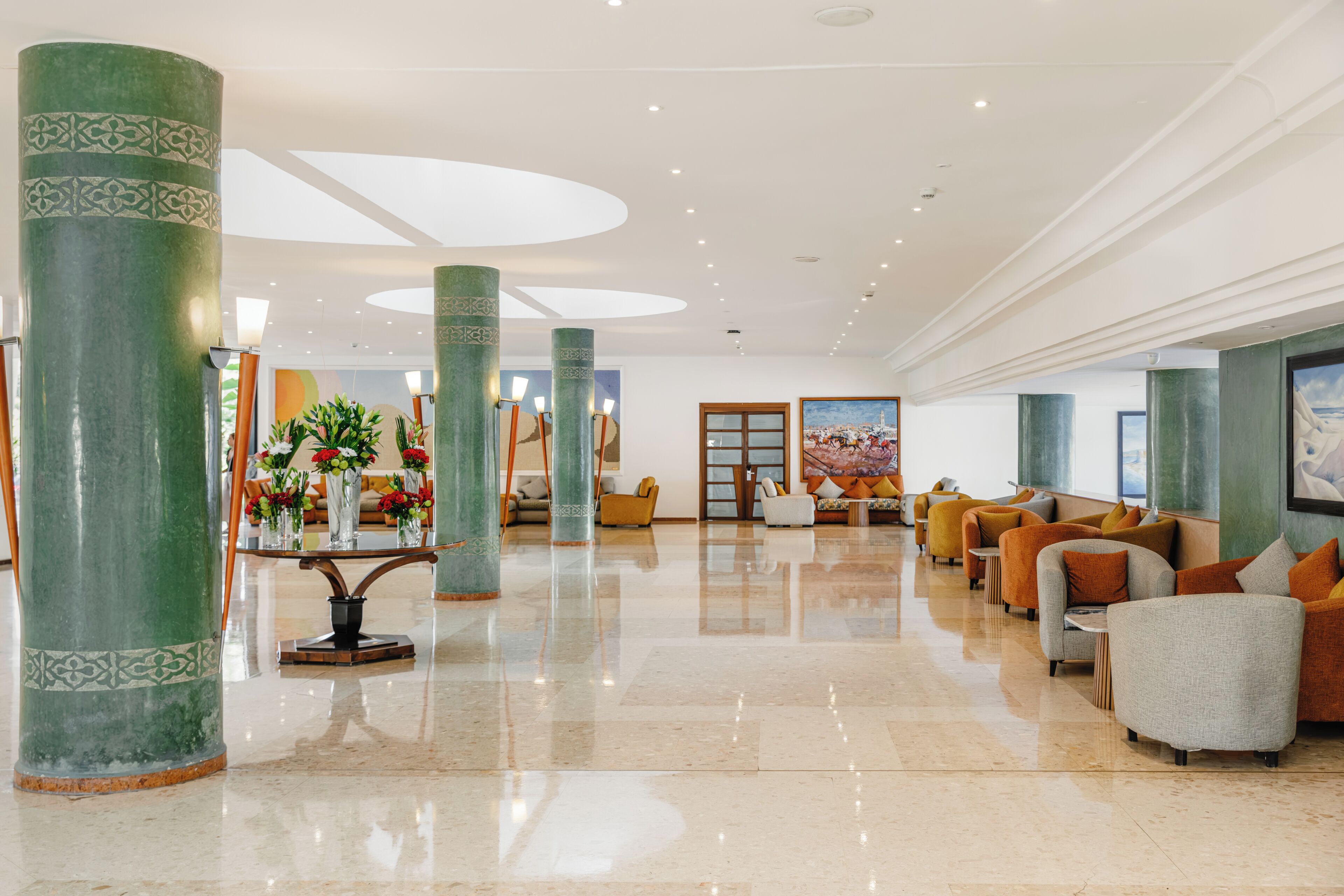 A spacious lobby with high ceilings, large green columns, and a seating area with sofas and armchairs.
