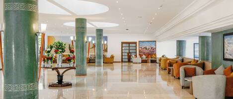 A spacious lobby with high ceilings, large green columns, and a seating area with sofas and armchairs.