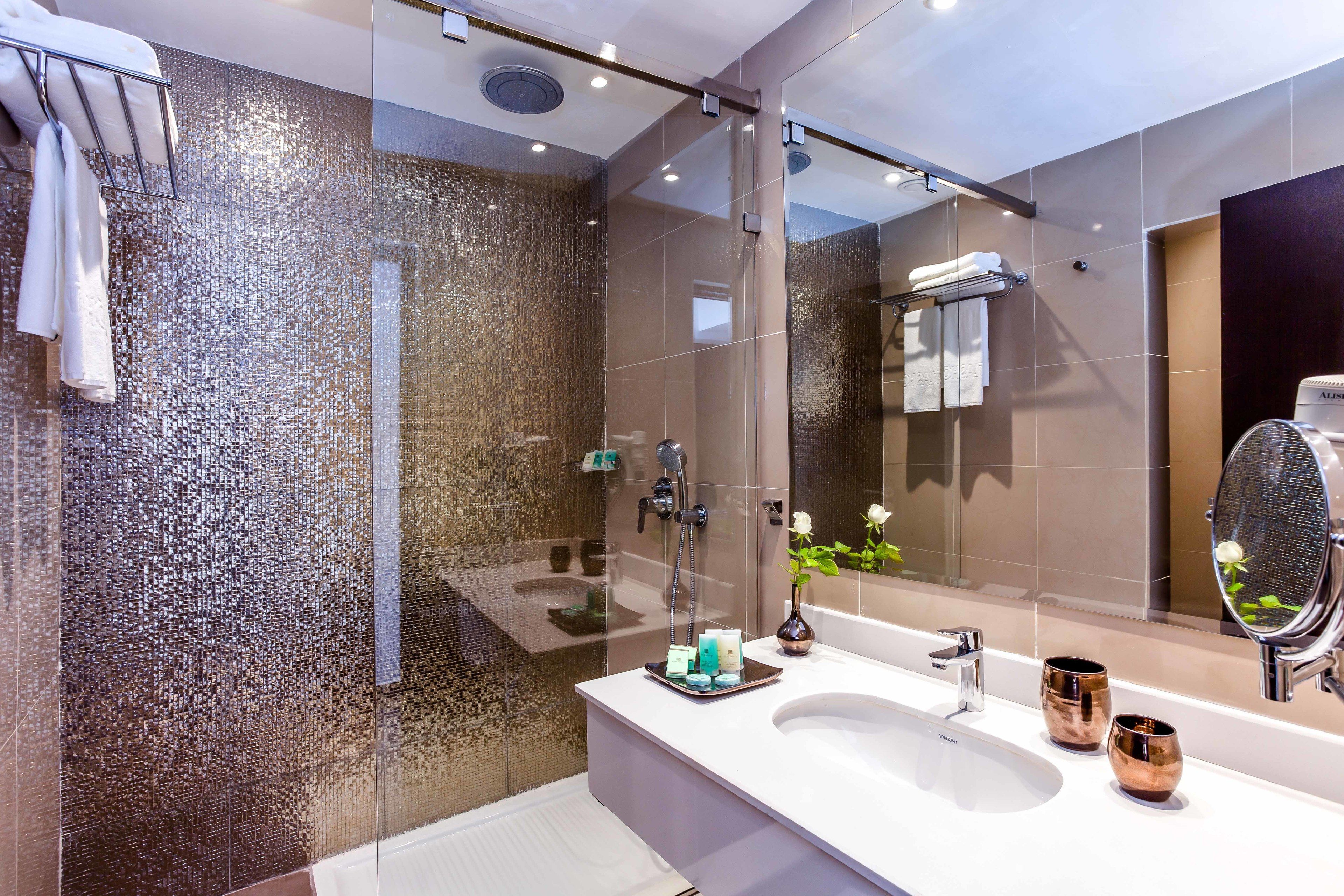 A modern bathroom with a glass shower enclosure, a large mirror, and a white sink with two copper mugs.