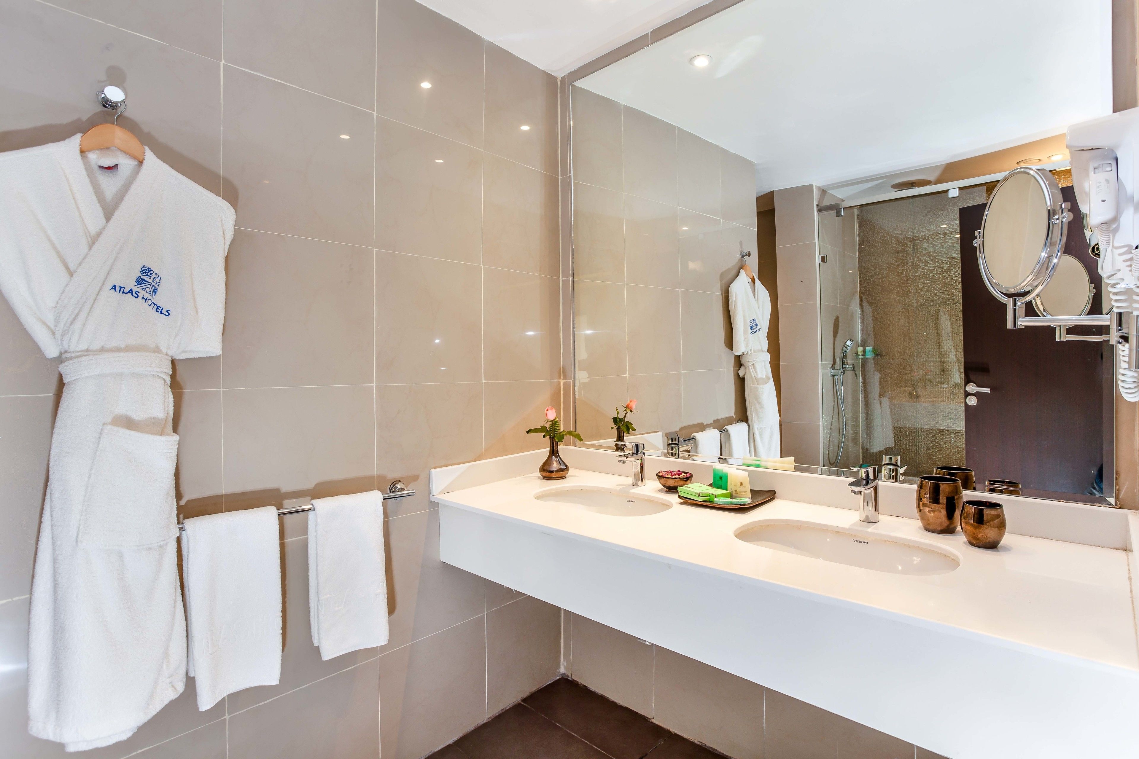 A modern bathroom with two sinks, a large mirror, and a robe hanging on a rack.