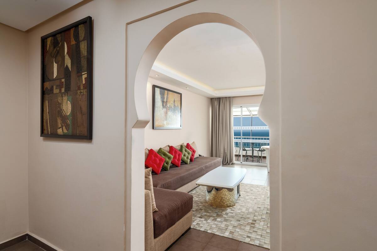 A modern living room with a brown sofa, a white coffee table, and a large painting on the wall.