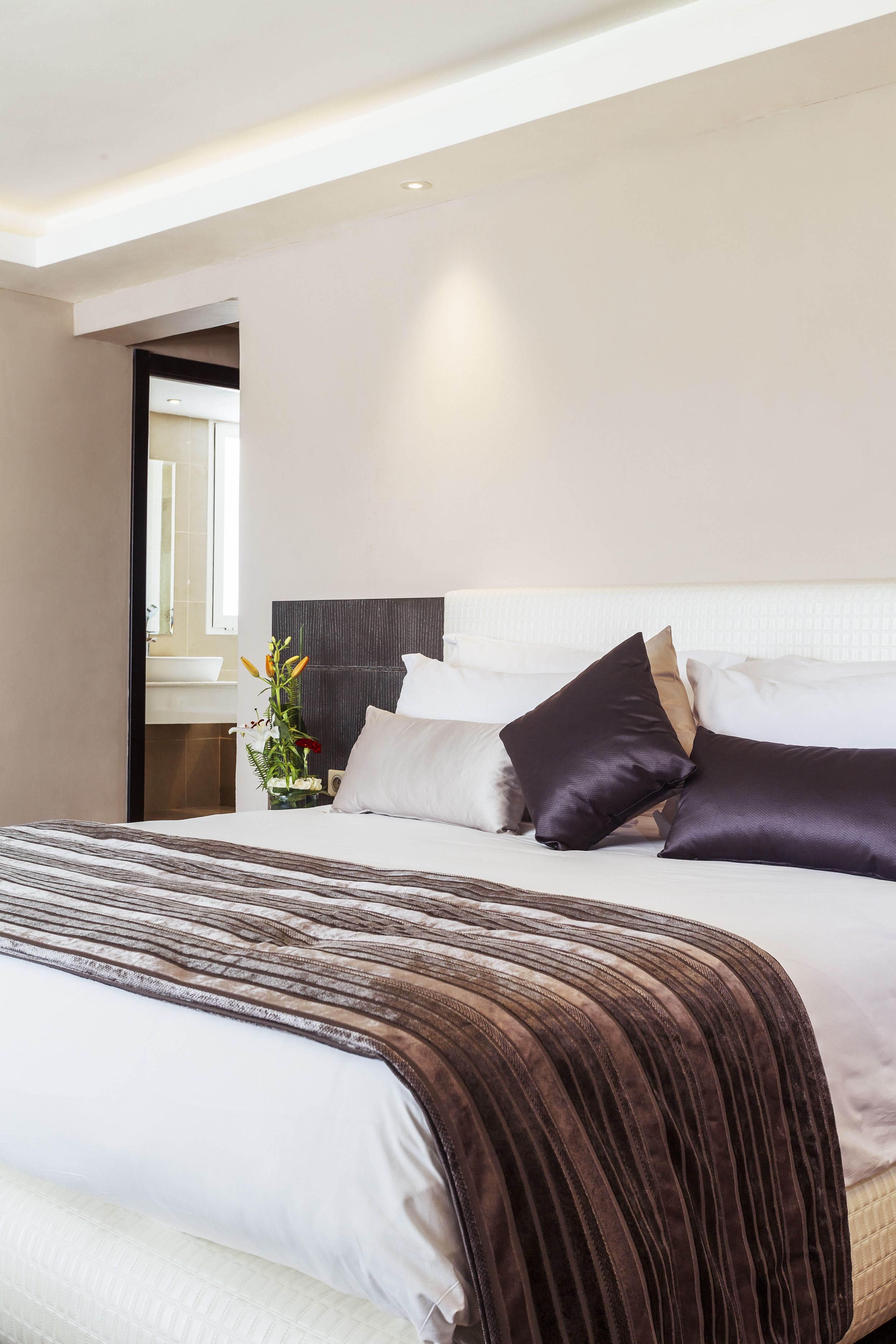 Una habitación de hotel moderna con una cama grande, una mesita de noche y un ventanal pequeño.