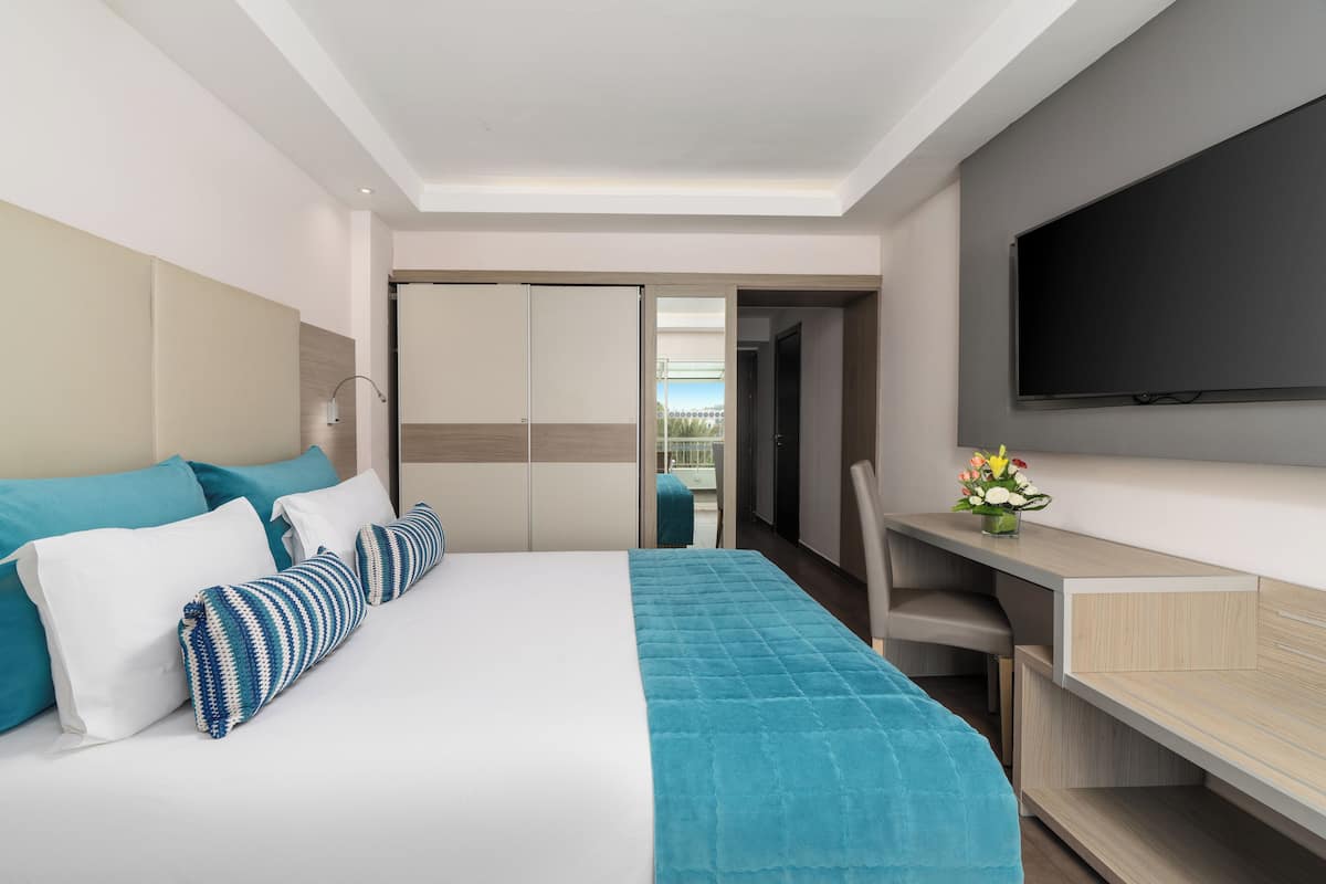 A modern hotel room with a bed, a desk, a TV, and a view of the outside.
