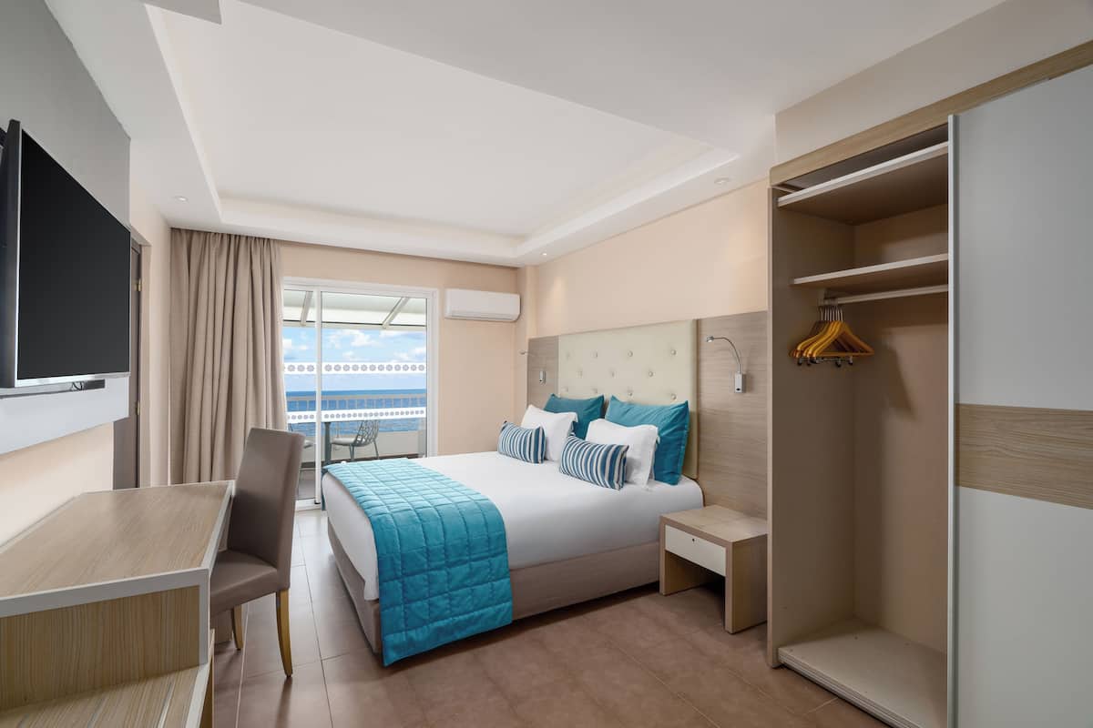 A modern hotel room with a bed, bedside table, and a desk with a chair.