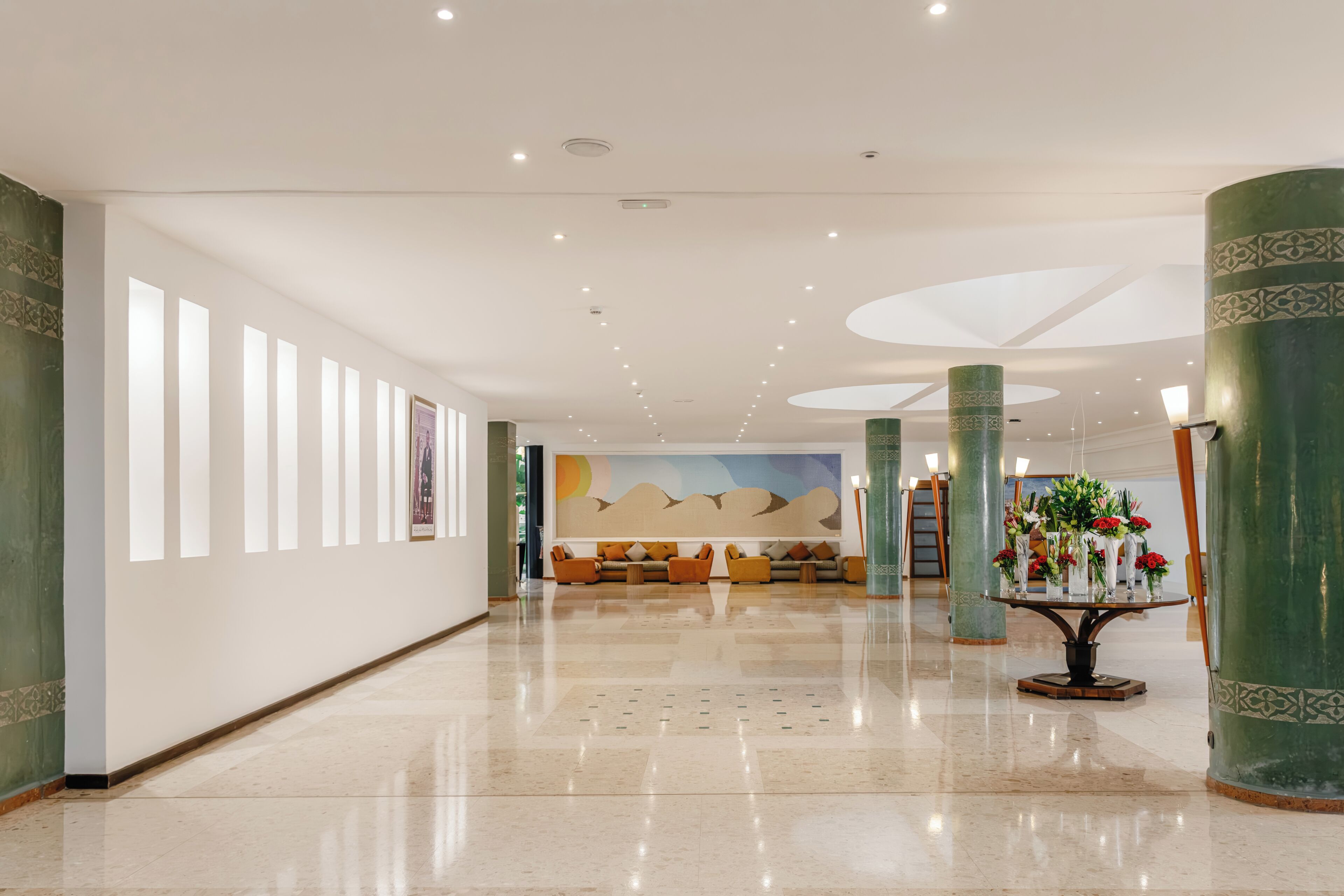 Een ruime lobby met een gepolijste marmeren vloer, een zithoek met banken en een decoratietafel met bloemen.