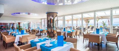 A spacious dining area with tables set for service, large windows offering views, and a modern ceiling design.