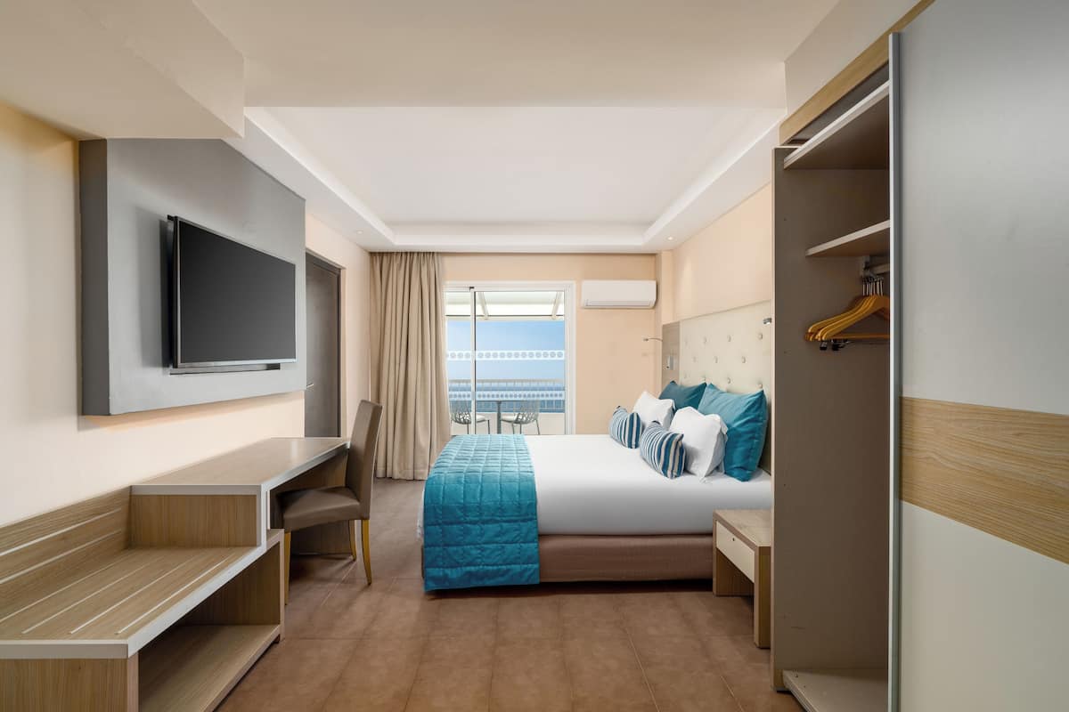 A hotel room with a bed, a desk, a chair, a TV, and a wardrobe.