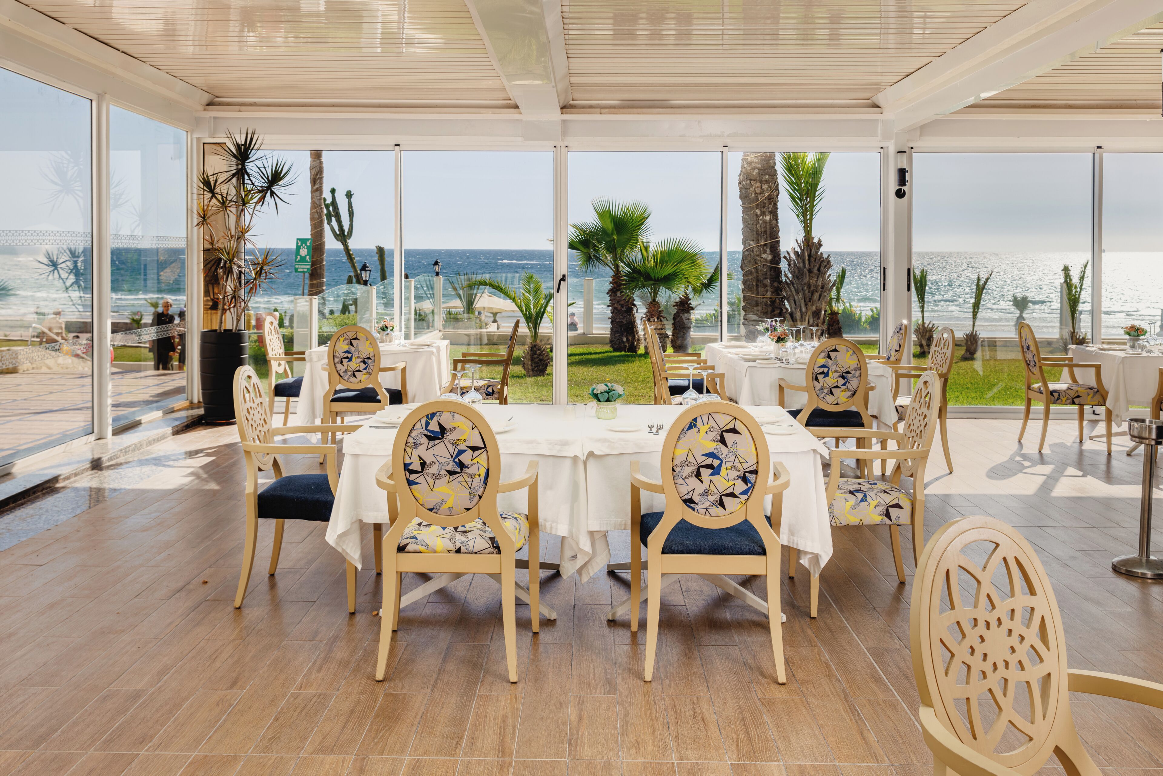Restaurante con terraza al aire libre que domina el mar, con sillas y mesas de madera y vistas panorámicas.