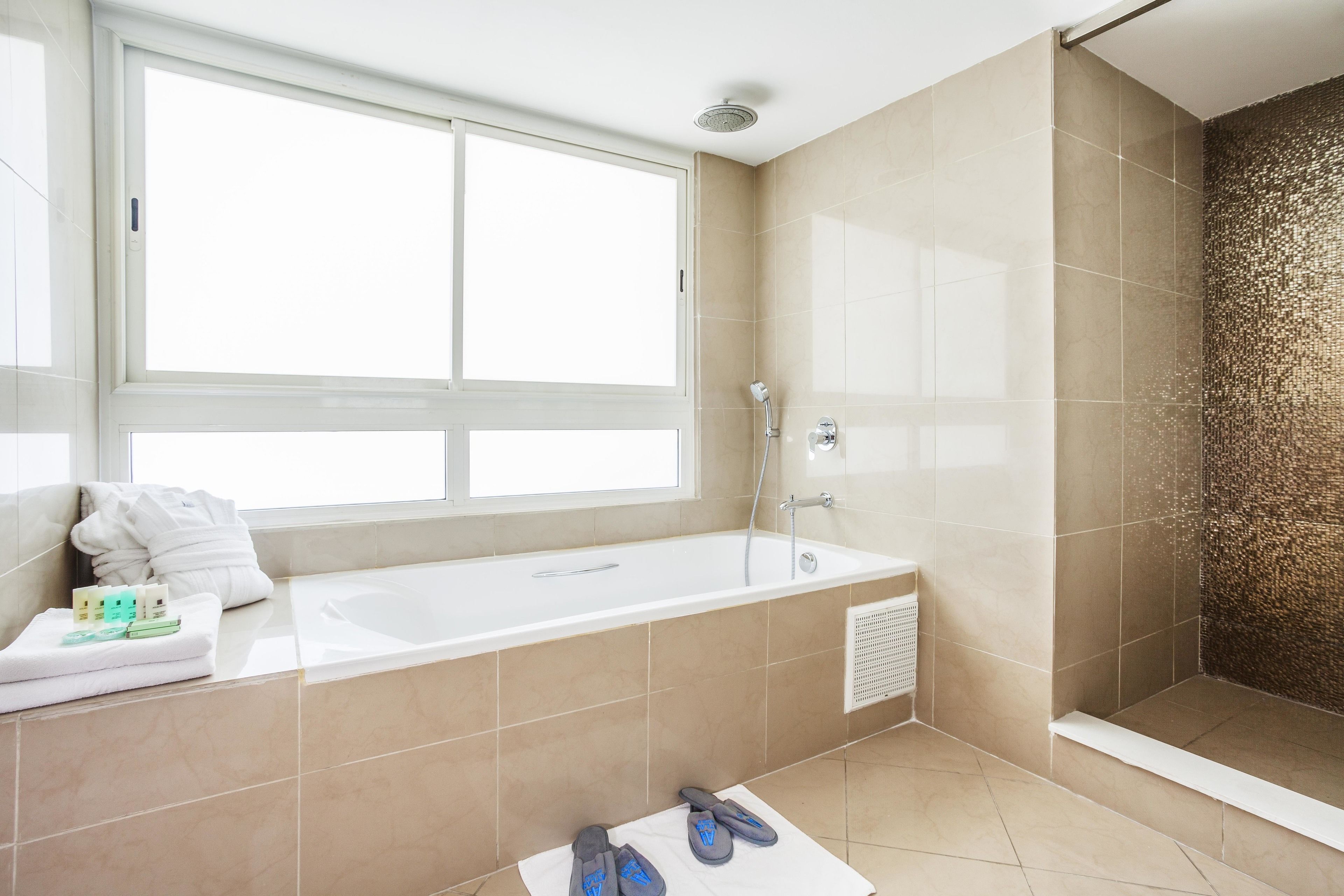A modern bathroom with a bathtub, shower, and a large window.
