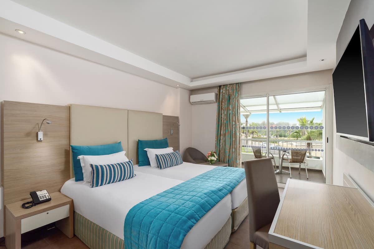 A hotel room with a bed, a desk, a chair, and a balcony with a view.