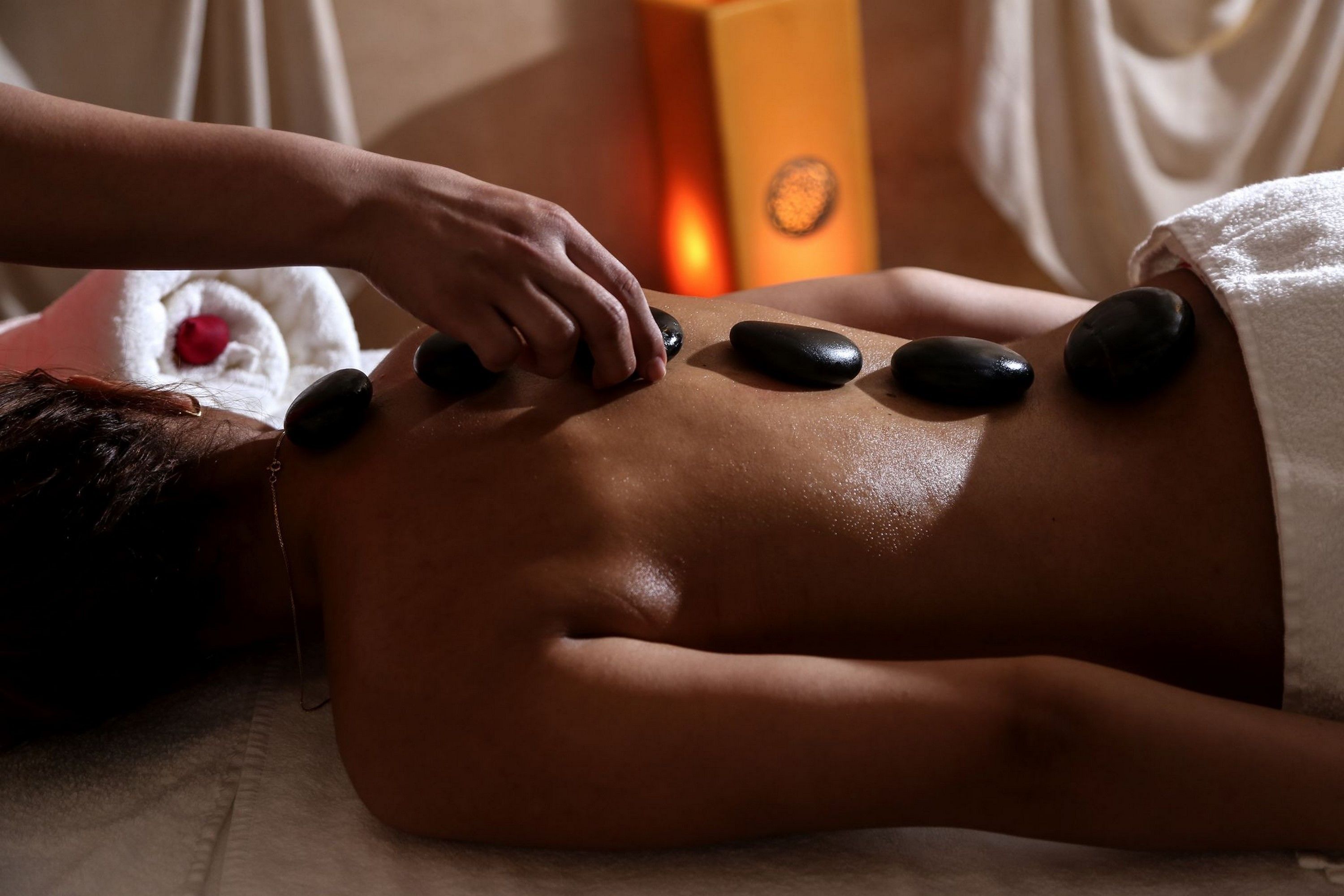 A person receiving a stone massage with a towel and a red flower on the side.