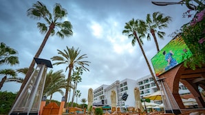 A resort with outdoor seating, palm trees, and a large screen displaying a game. - Hotel Argana (Agadir)