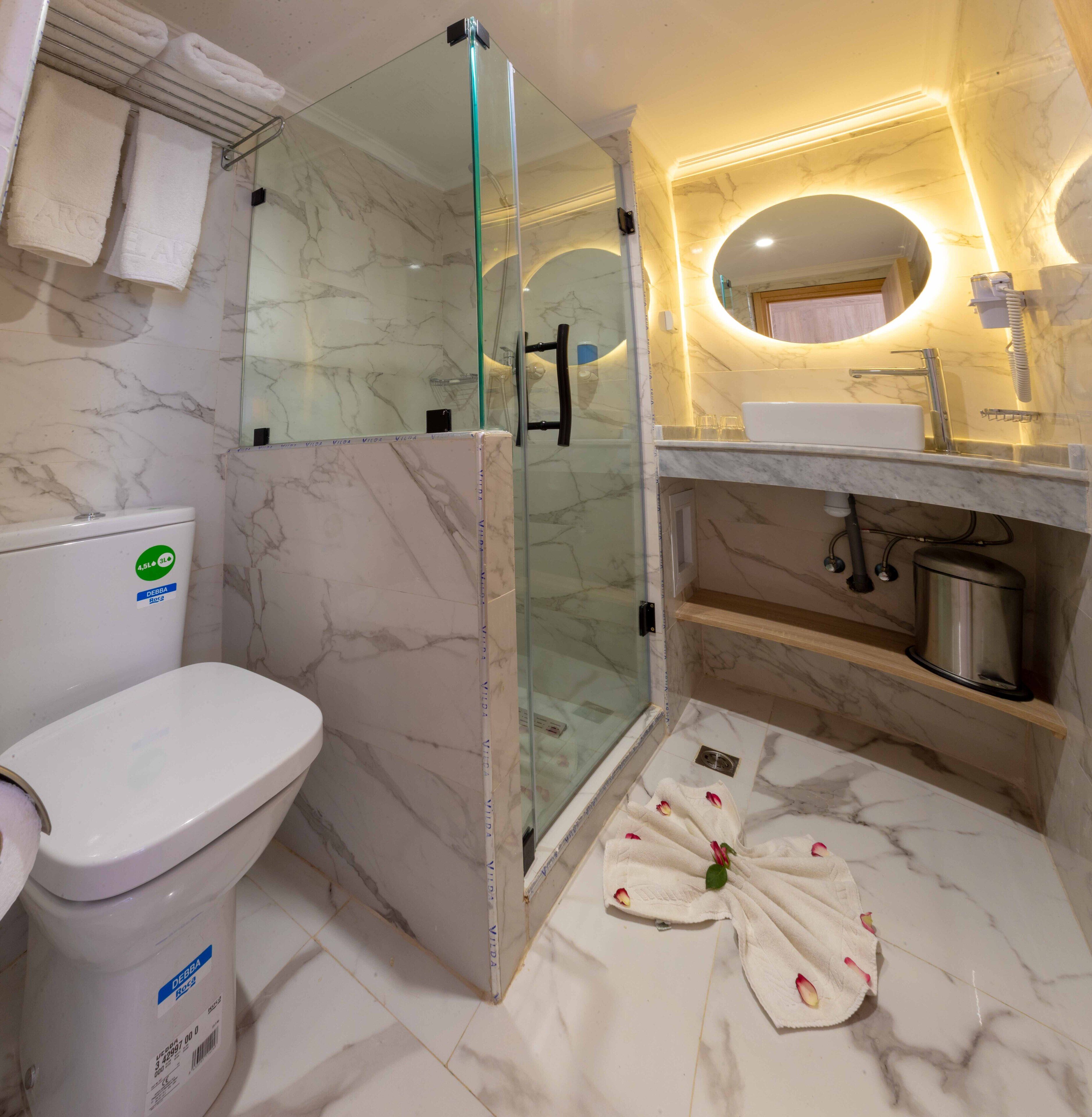 Un baño con ducha de vidrio, inodoro y lavamanos con encimera de mármol.