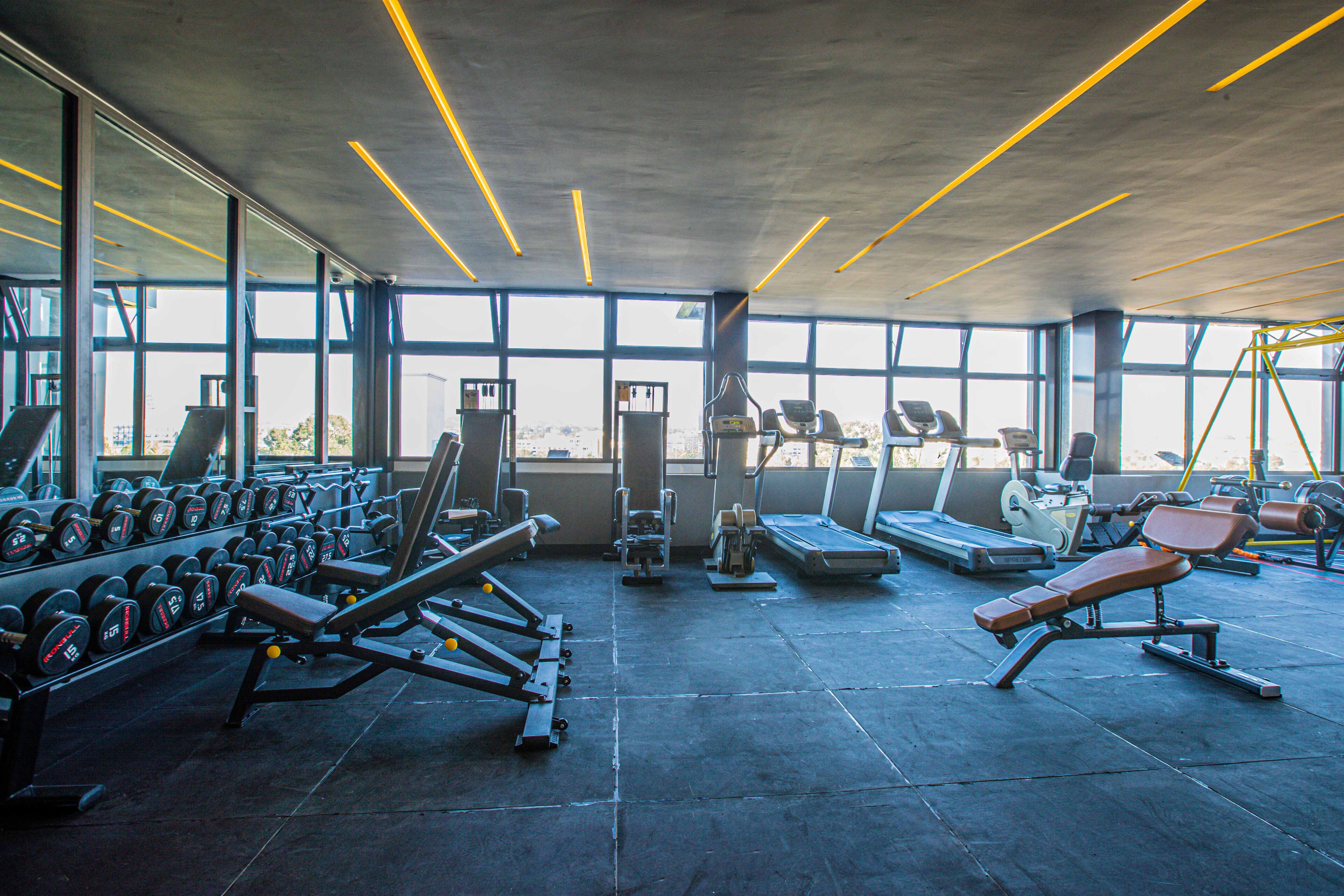 A gym with various exercise equipment, large windows, and a concrete ceiling.