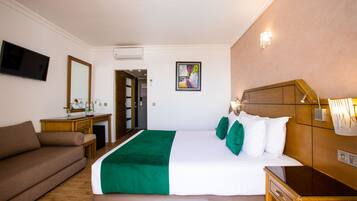 A hotel room with a bed, a sofa, a desk, a TV, and a painting on the wall.