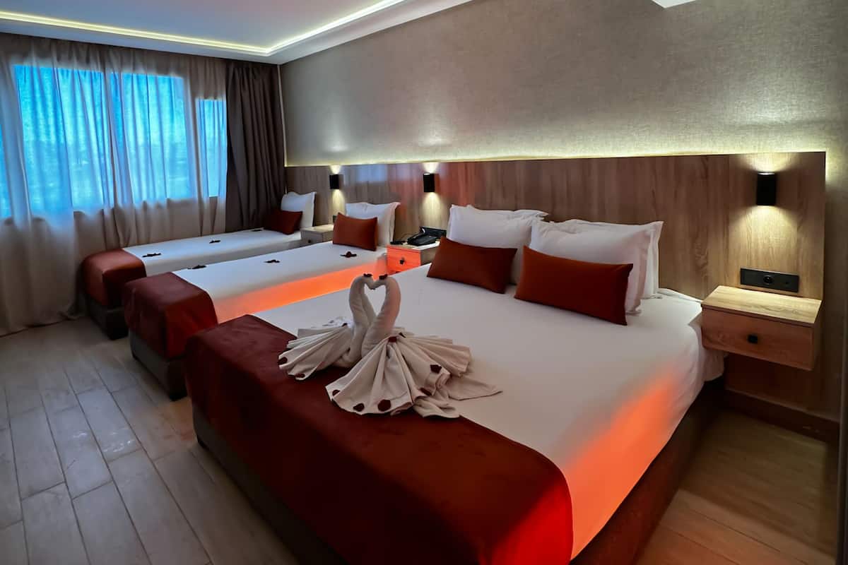 A hotel room with two beds, a wooden headboard, bedside tables, and a decorative swan on the beds.