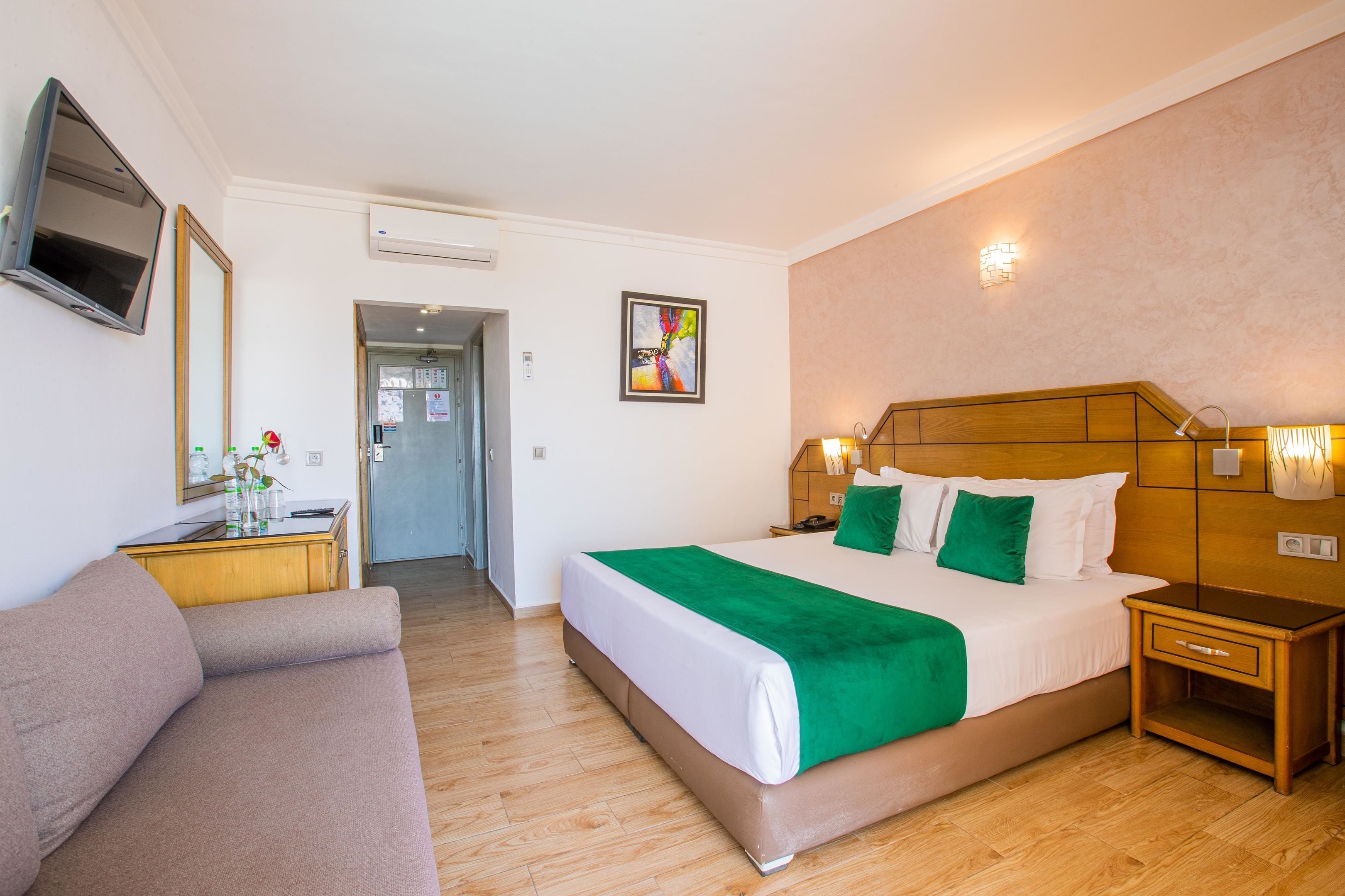 Hotellihuone, jossa on sänky, puinen pääty, yöpöytä, televisio ja sohva.