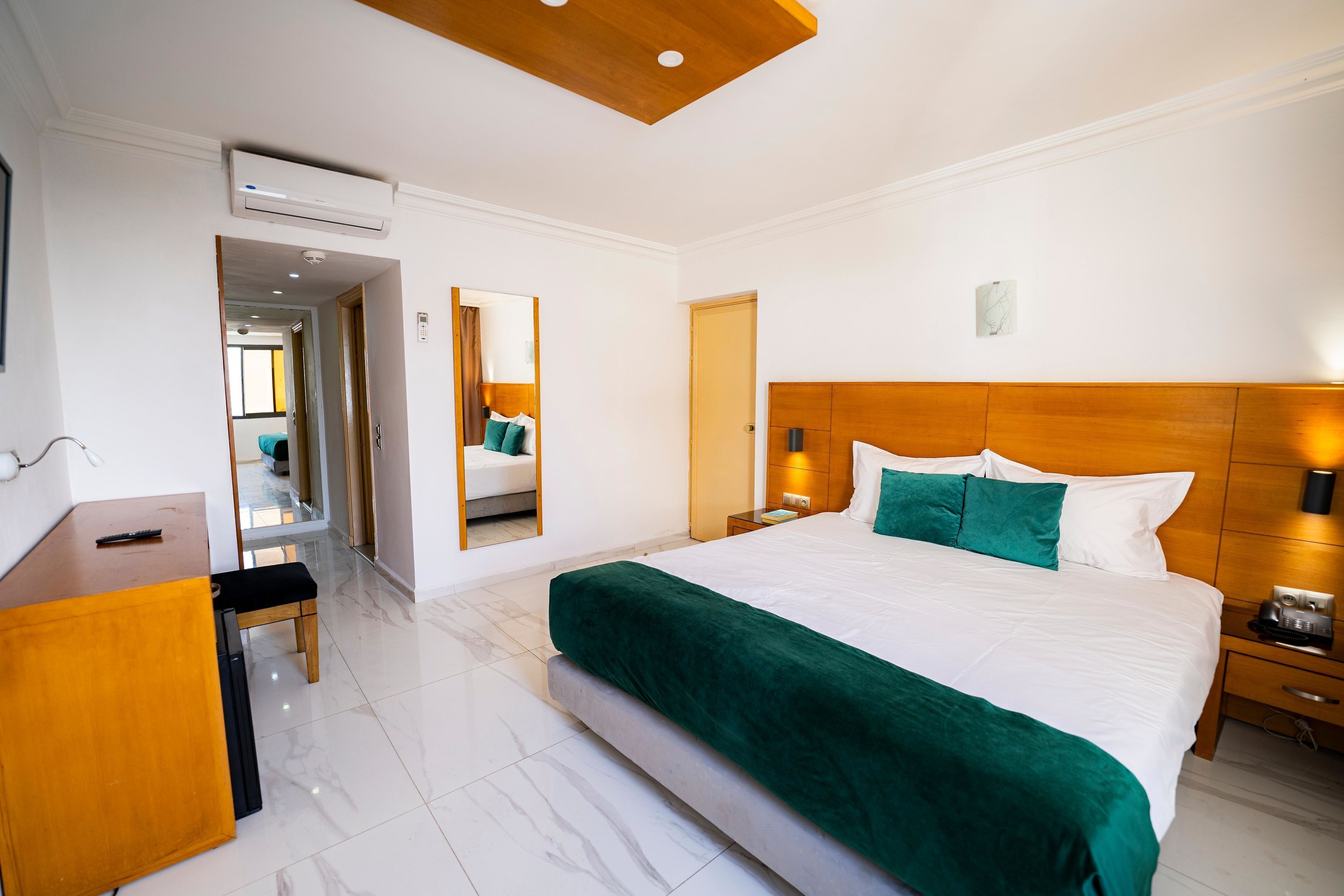 A modern hotel room with a large bed, a wooden headboard, a desk, and a mirror.