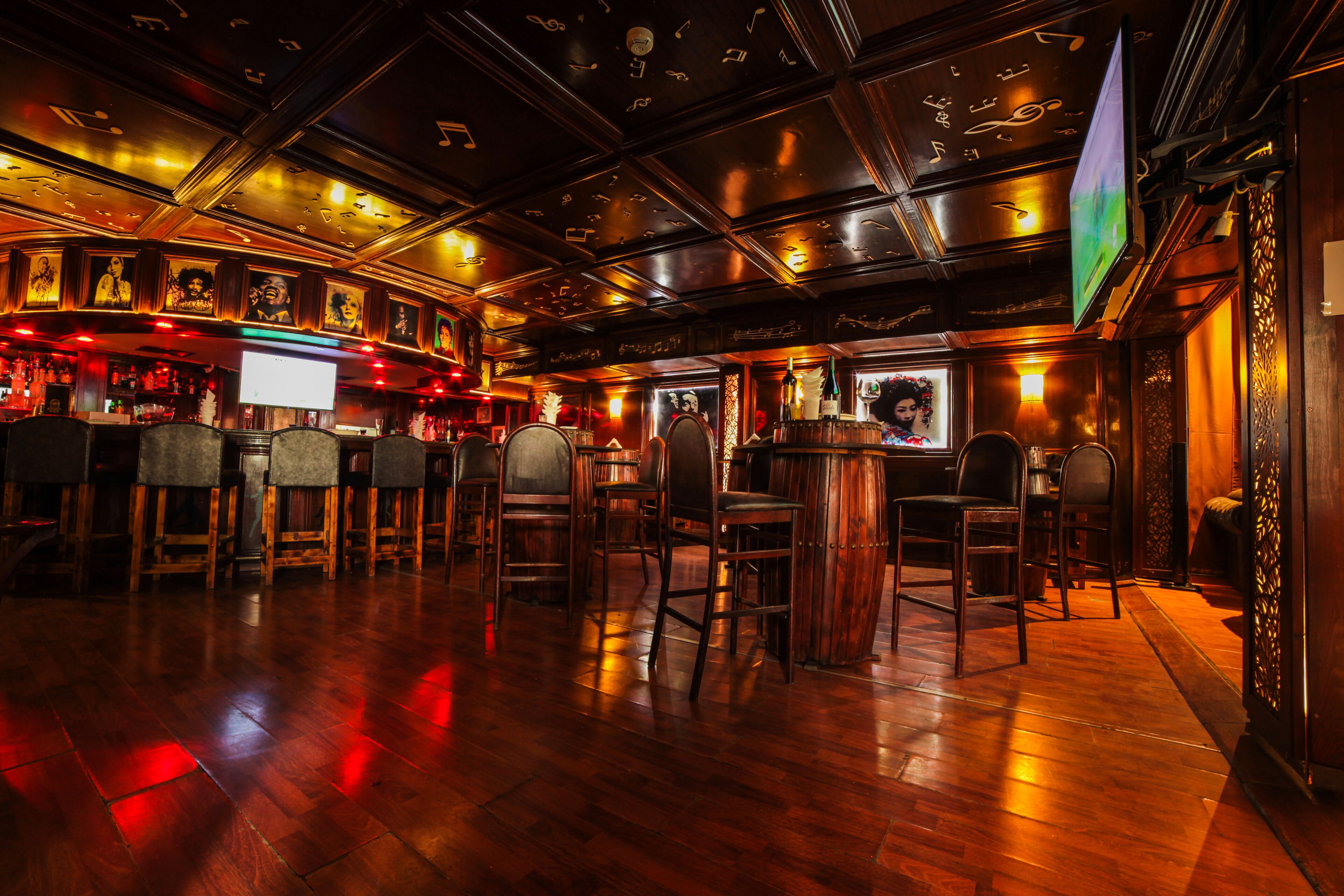 A bar area with wooden flooring, bar stools, and a television screen.