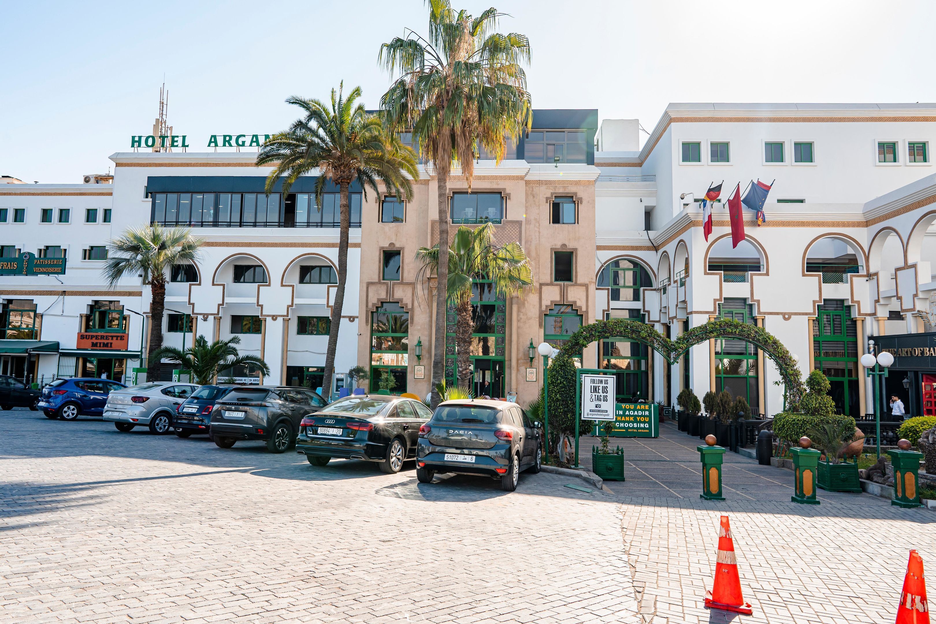 Een hotel met een moderne gevel, meerdere balkons en een parkeerplaats met verschillende auto's.