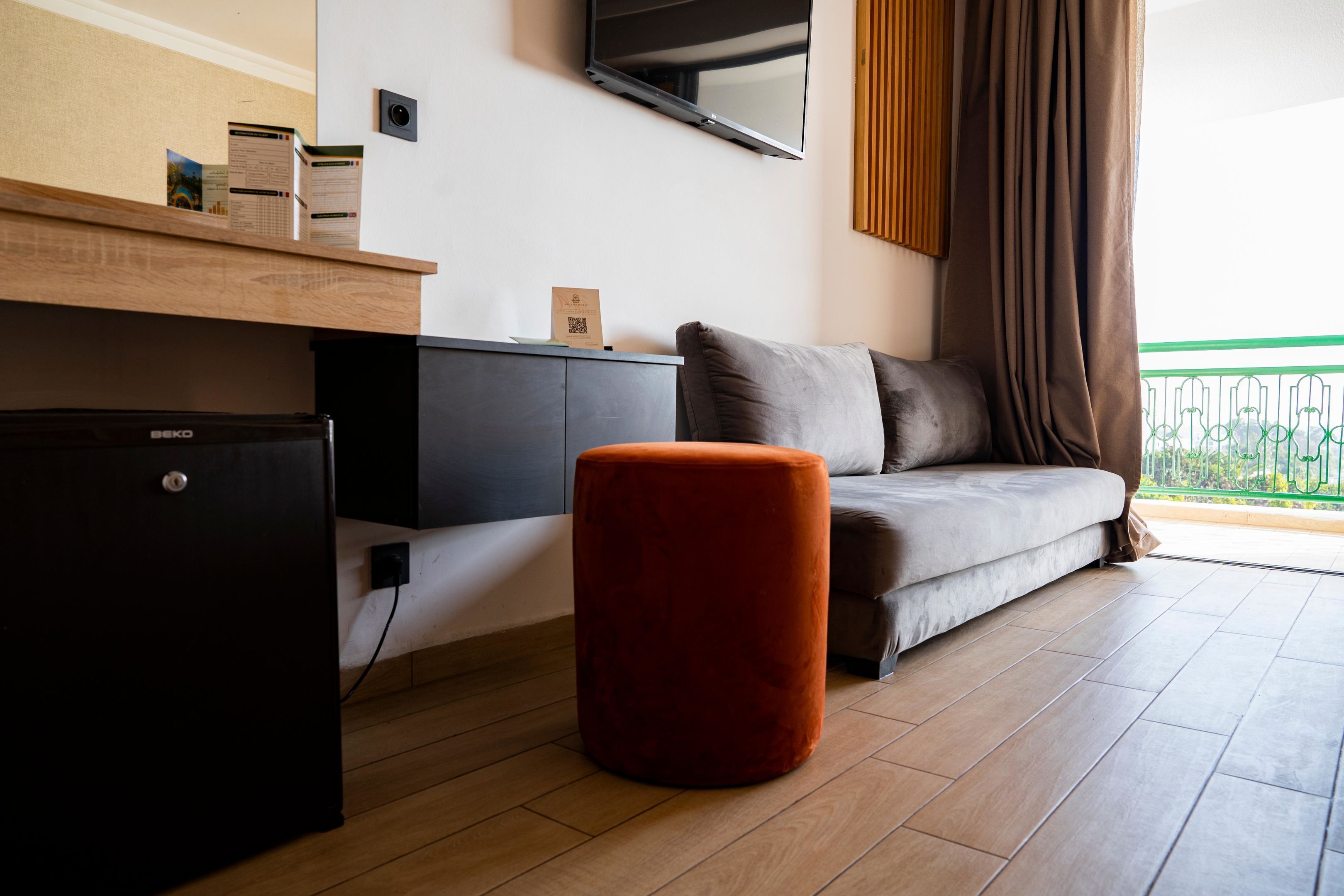 En moderne stue med sofa, skammel og et lille, sort køleskab.