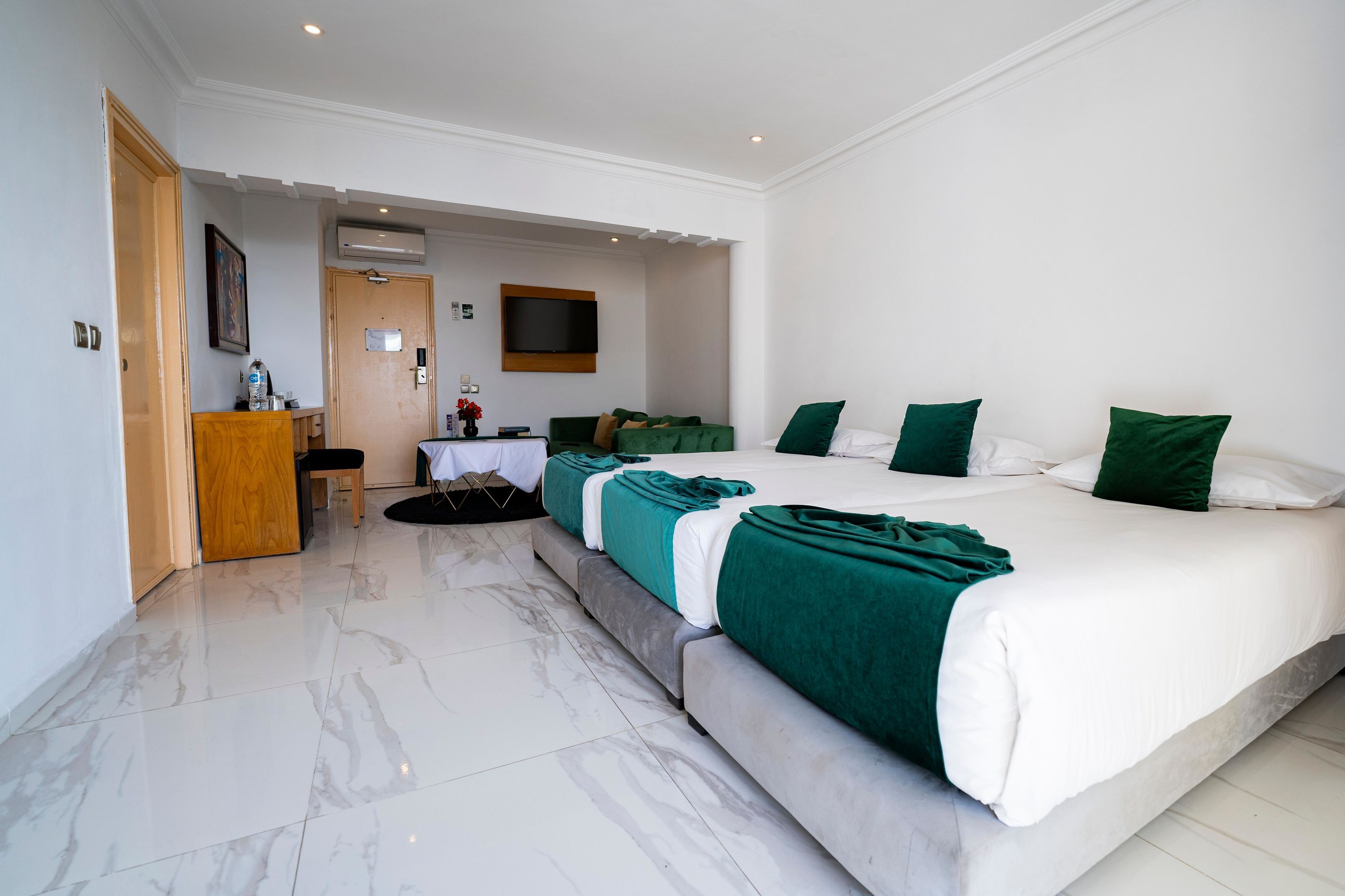 A hotel room with a large bed, a desk, a chair, a TV, and a door.