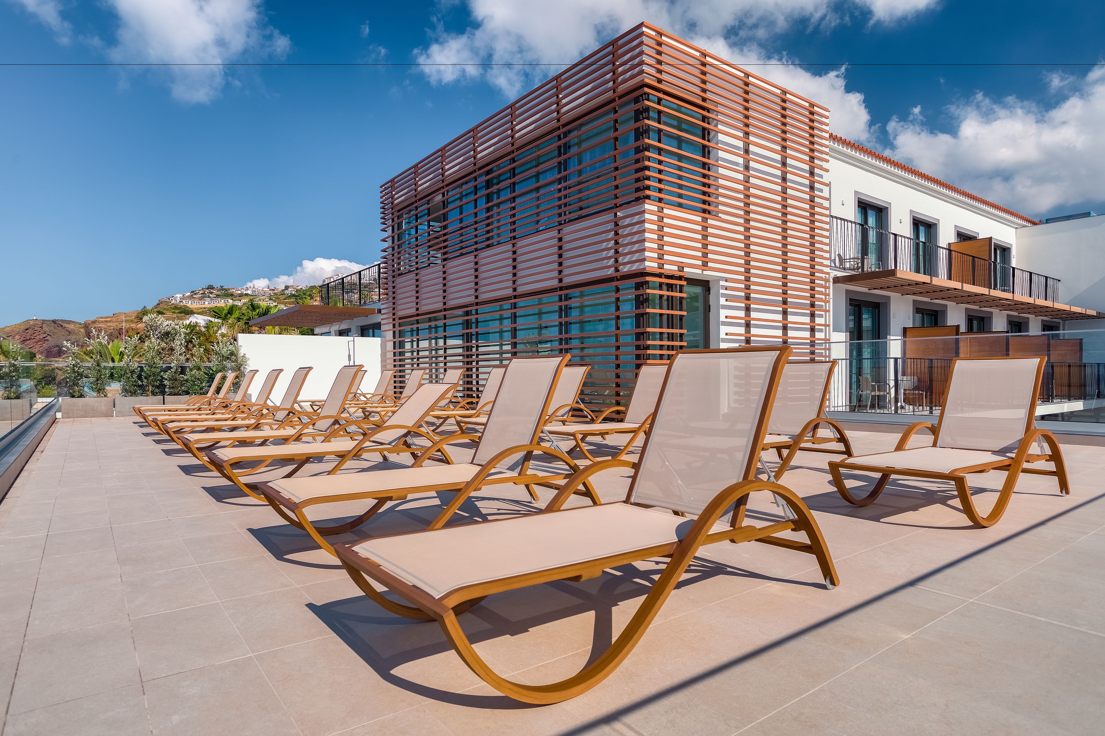 Un bâtiment moderne doté d’une terrasse avec des chaises longues et offrant une vue sur une colline.