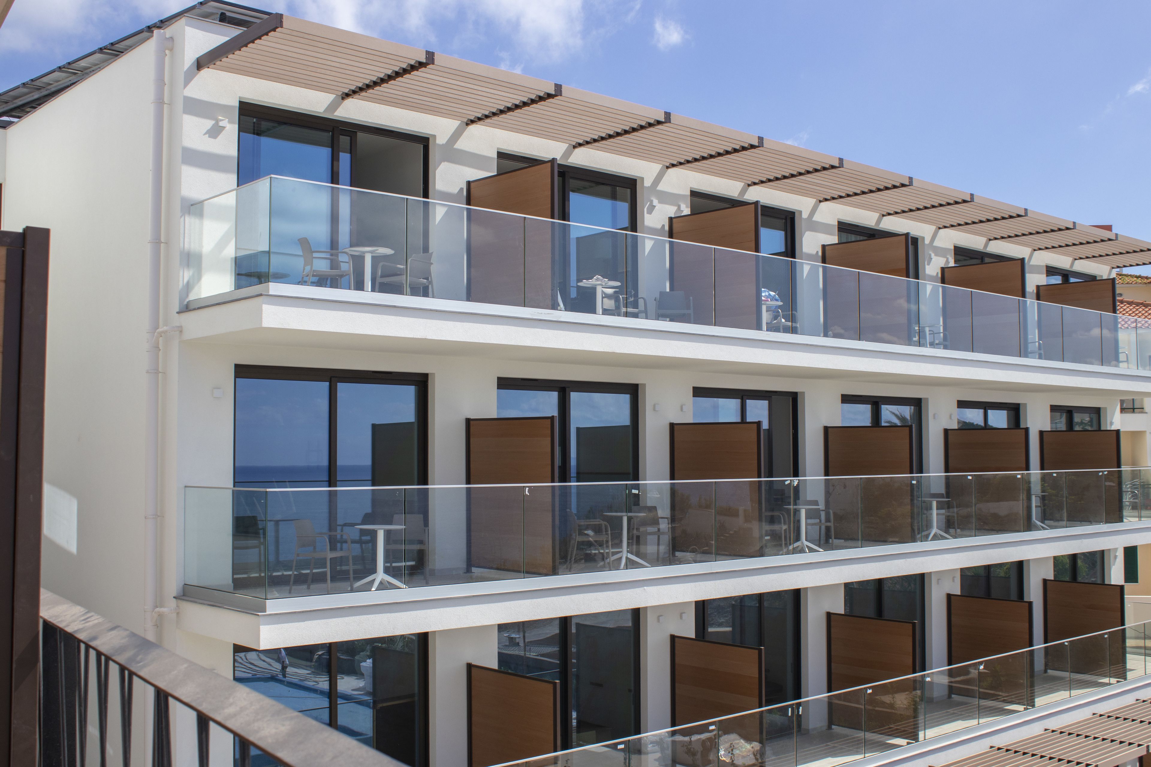 Un hotel moderno con un balcón de dos pisos, amplias ventanas y vistas al mar.